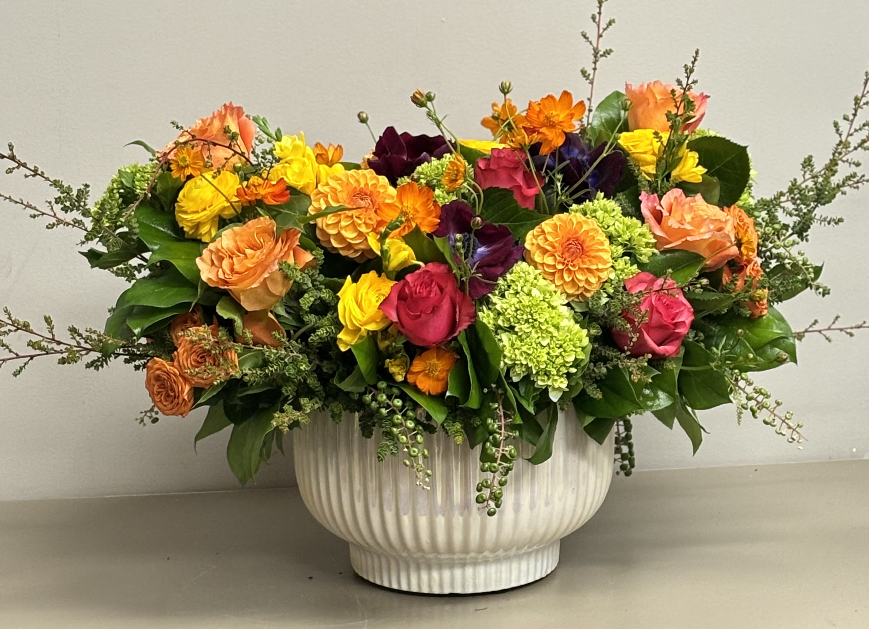 Low centerpiece of bright roses, dahlias, and green hydrangeas in a white ceramic bowl