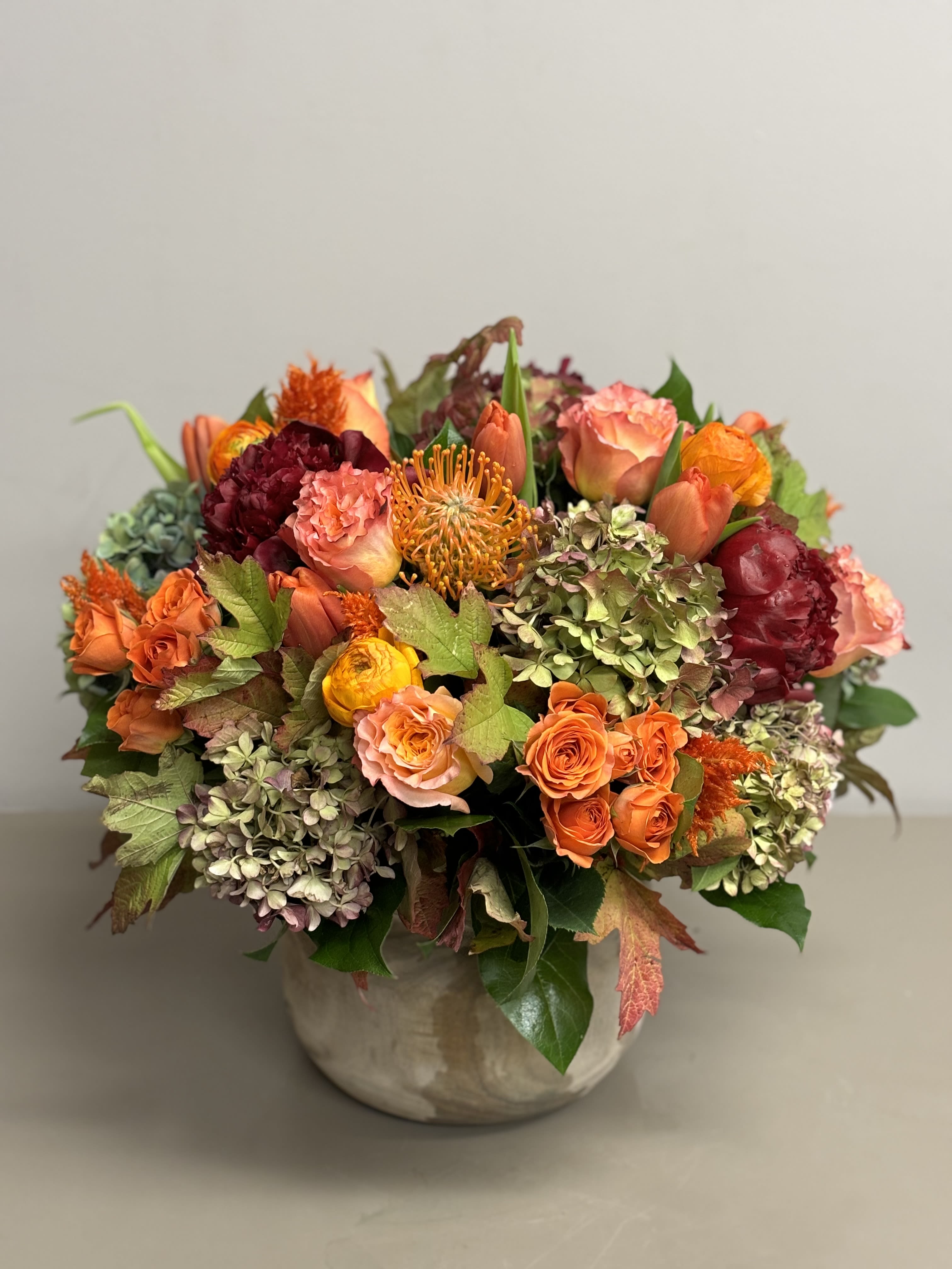 Low ceramic vase of orange and peach roses, hydrangeas, and mixed warm-toned flowers