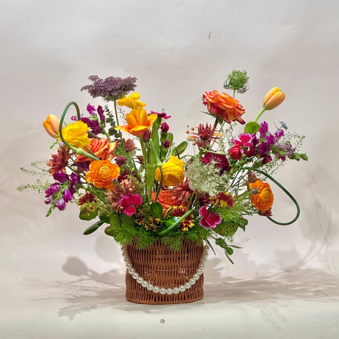Colorful mixed flower arrangement in a wicker basket with a pearl garland