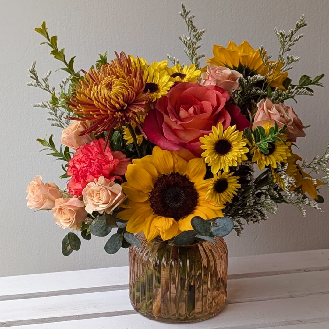 Mixed bouquet with sunflowers, roses, and mums in a ribbed glass vase