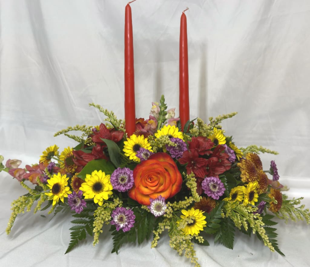 Floral centerpiece with two red taper candles and mixed blooms in a low arrangement