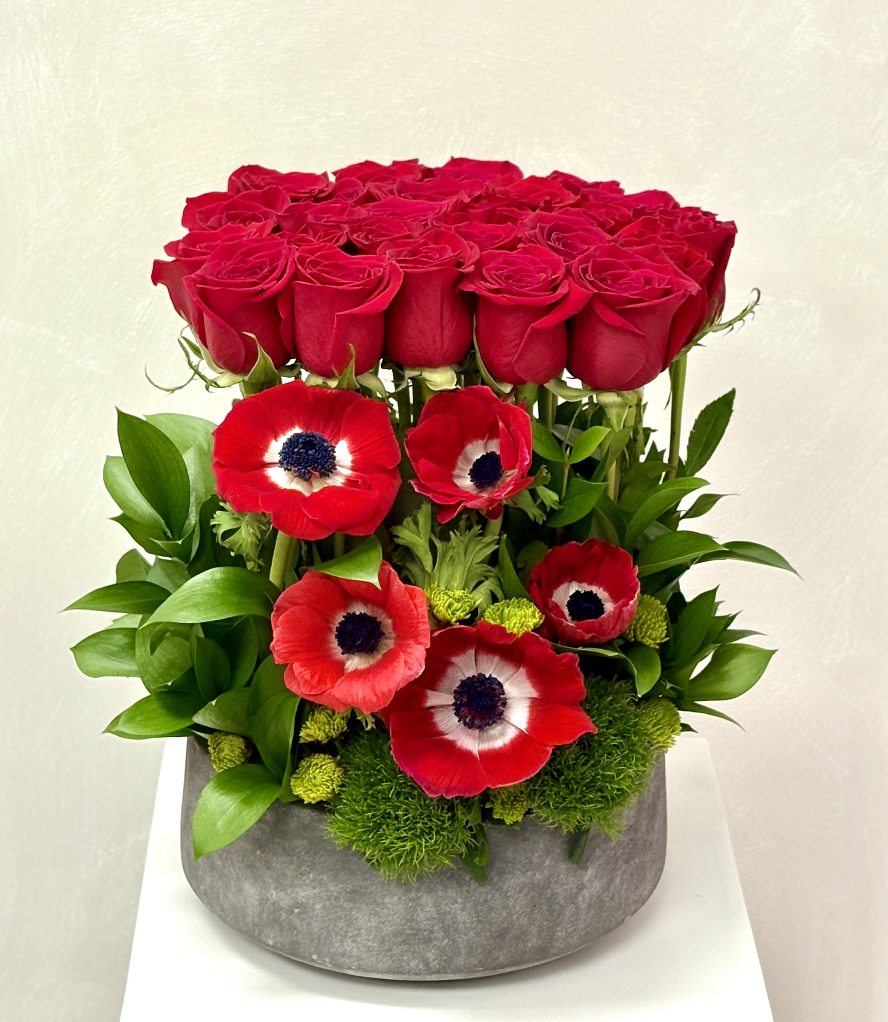 Red roses and red anemones arranged in a gray vase