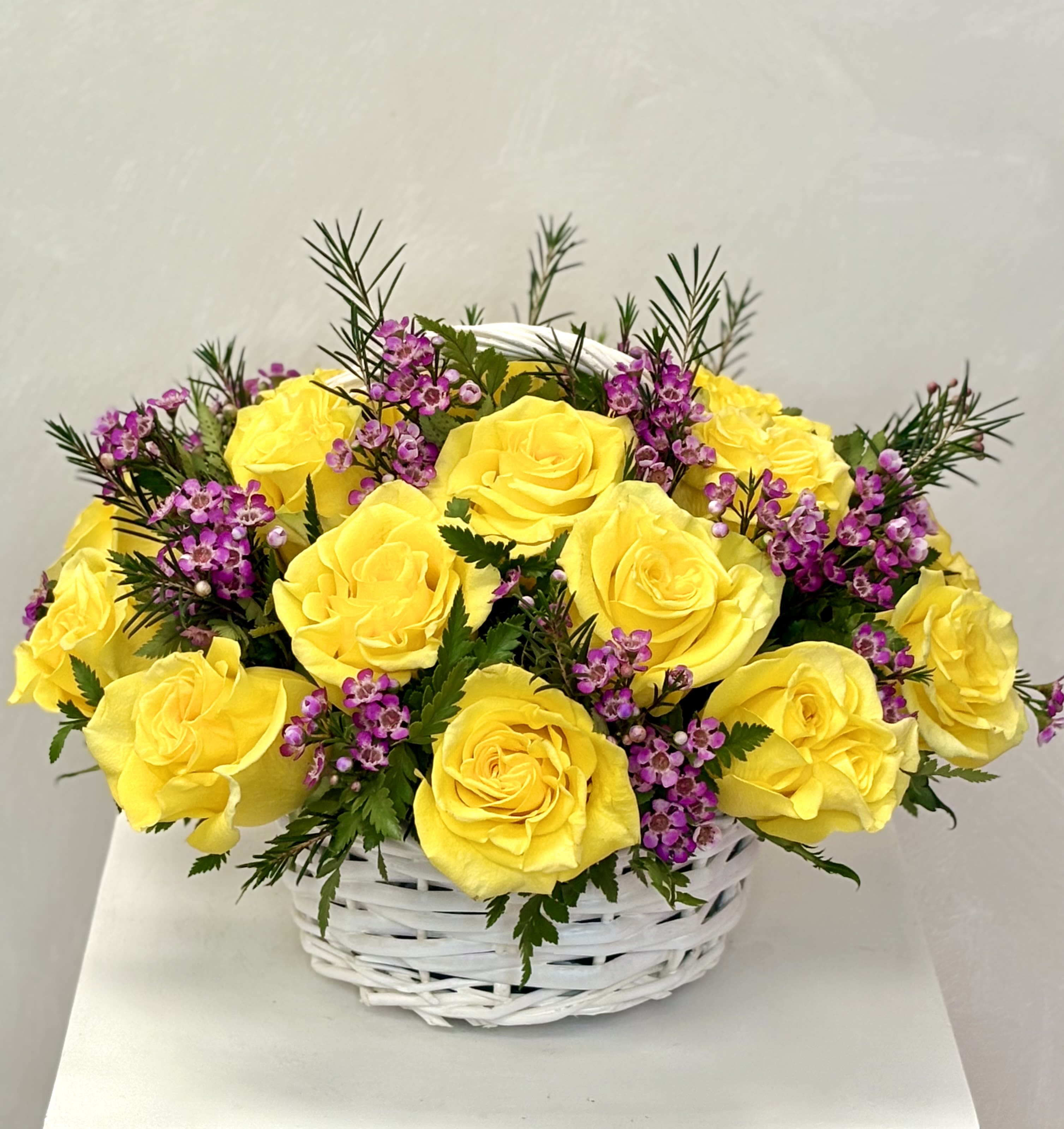 Yellow roses and purple filler flowers in a white basket