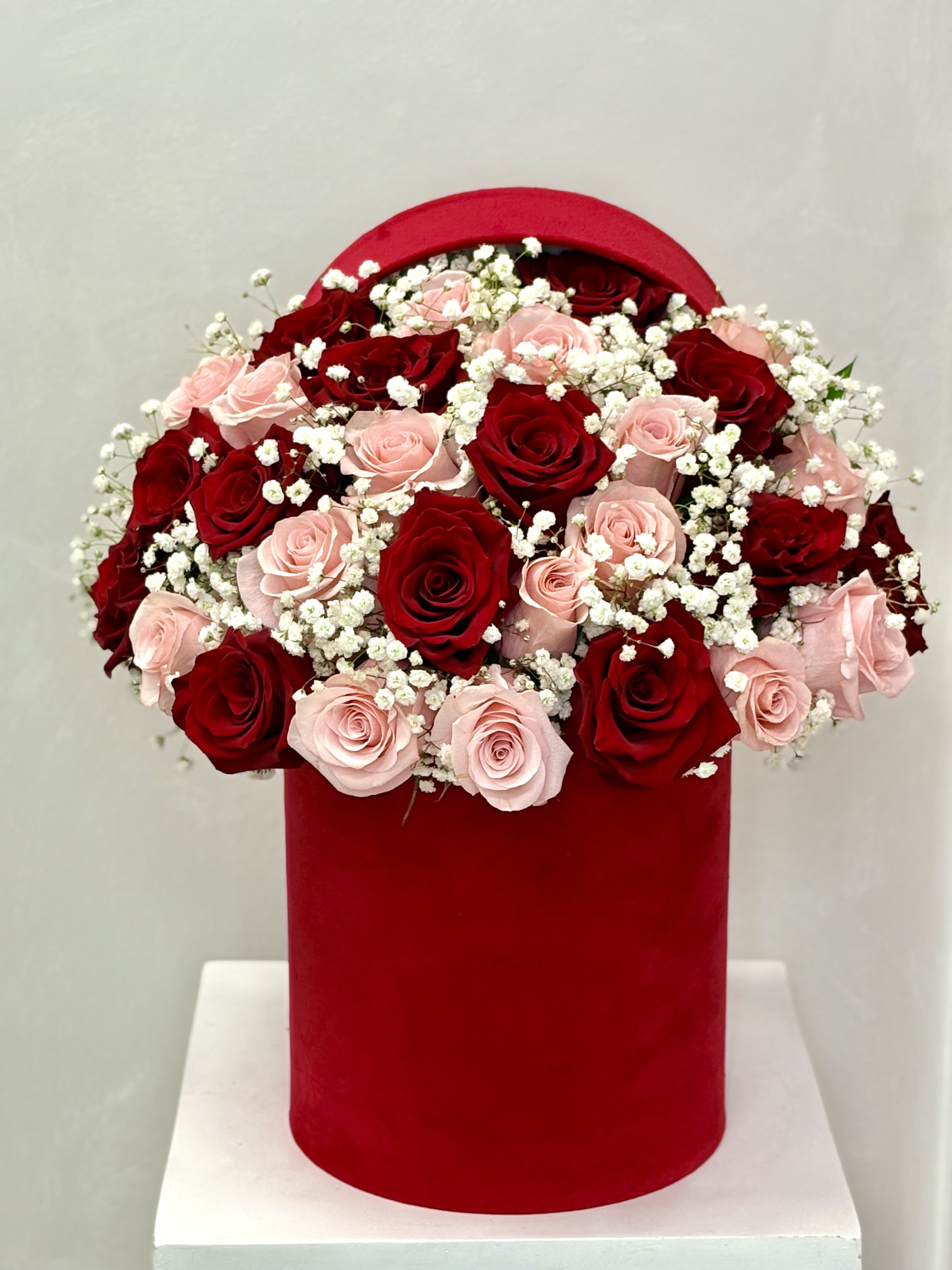 Red and blush roses arranged in a red hat box