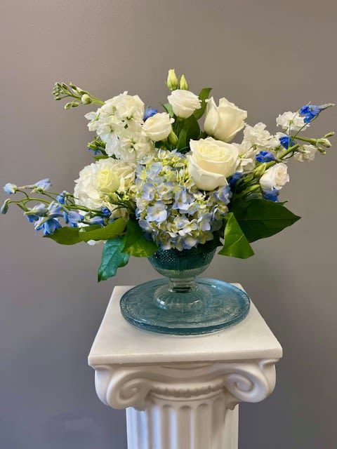 White and blue floral arrangement in a blue glass vase