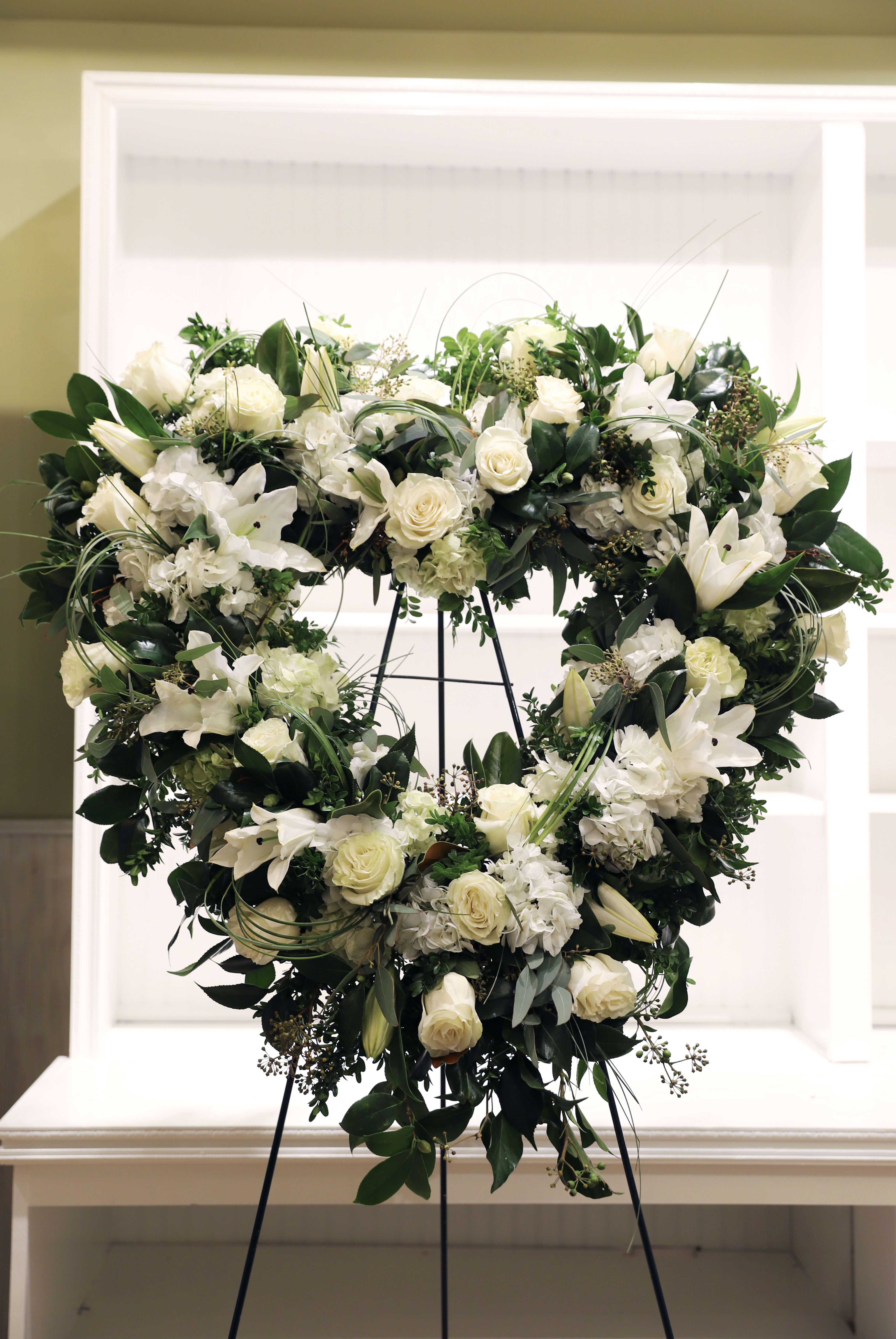 Heart-shaped standing wreath of white roses, lilies, and hydrangeas on a metal easel