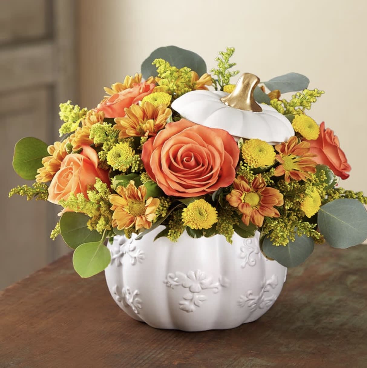 Orange and yellow flower arrangement in a white pumpkin vase
