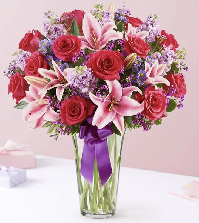 Pink roses and lilies arranged in a clear glass vase with a purple ribbon