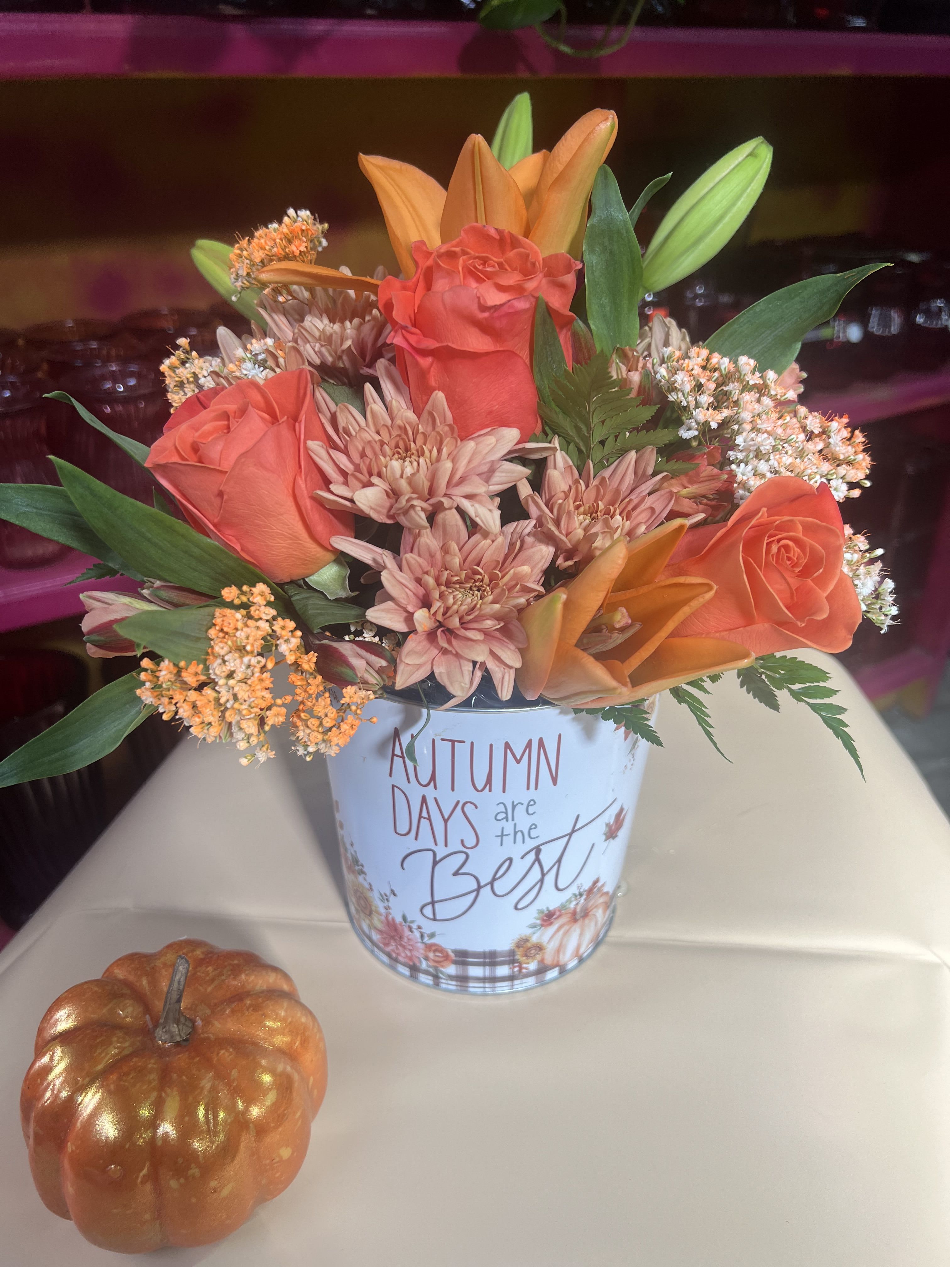 Autumn floral arrangement in a printed tin with orange roses and lilies