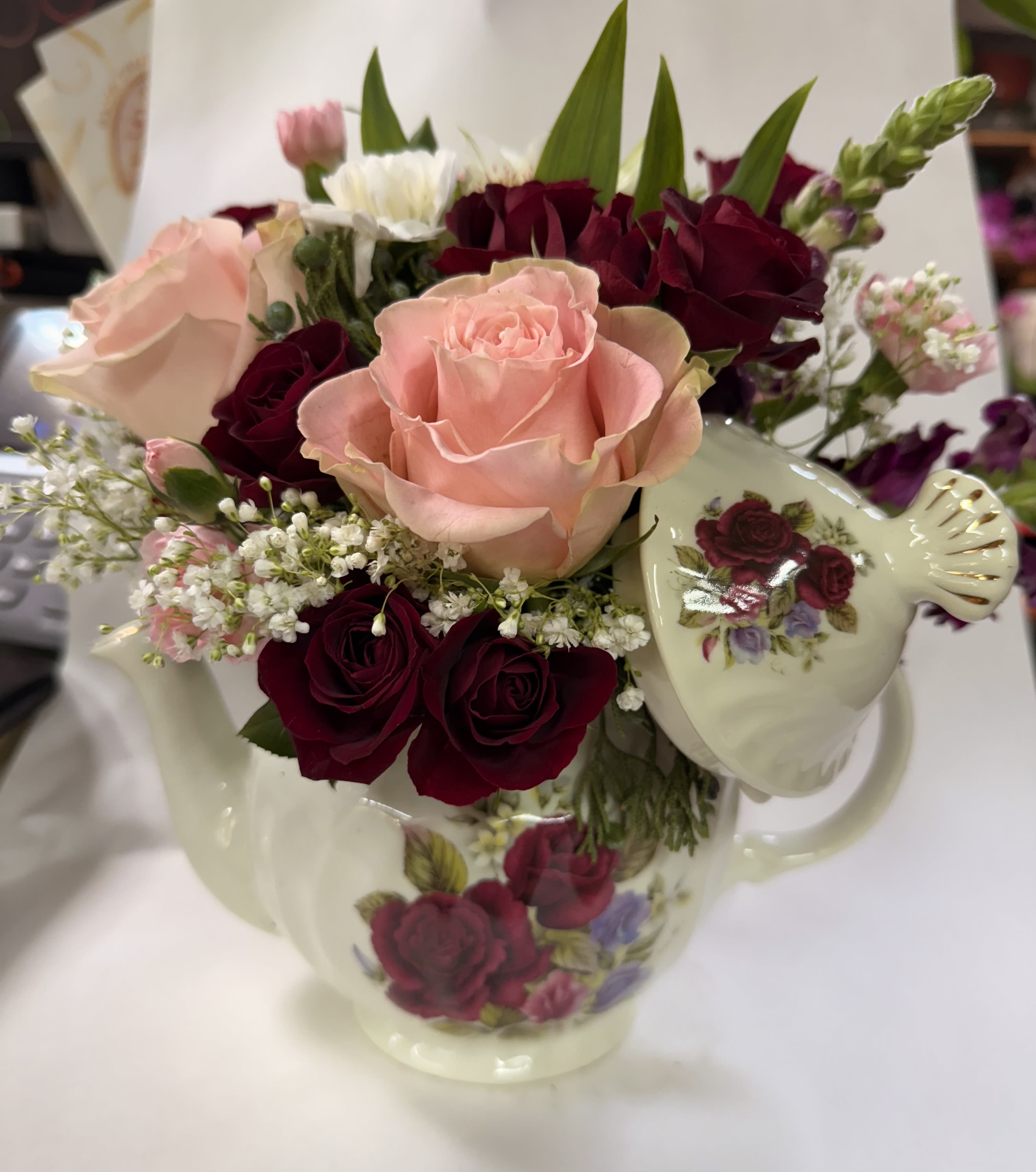 Pink and burgundy roses arranged in a floral teapot