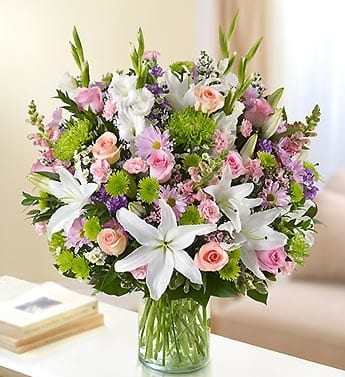 Mixed bouquet of white lilies, pink roses, and green mums in a glass vase