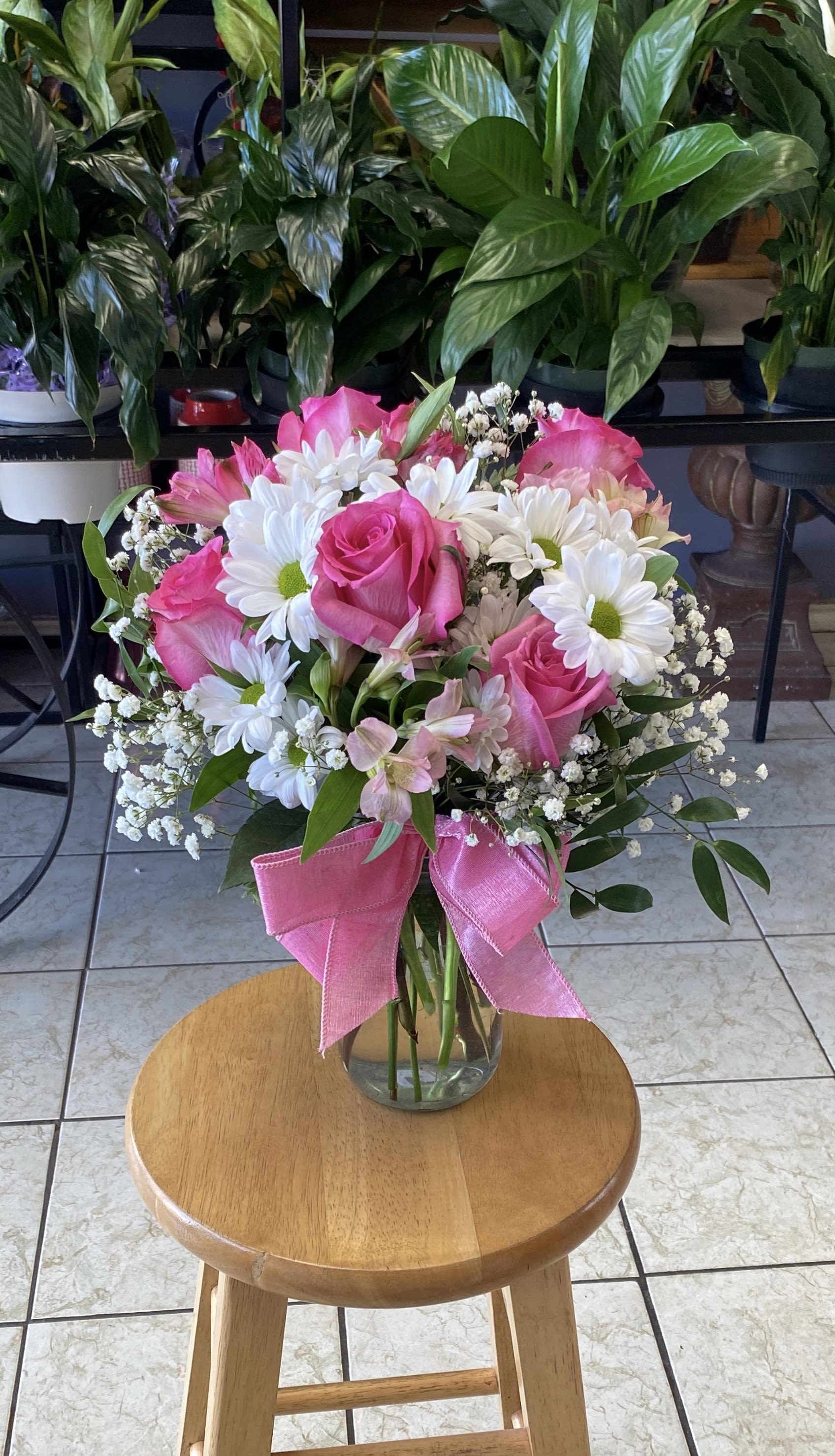 Pink roses and white daisies arranged in a glass vase with a pink ribbon