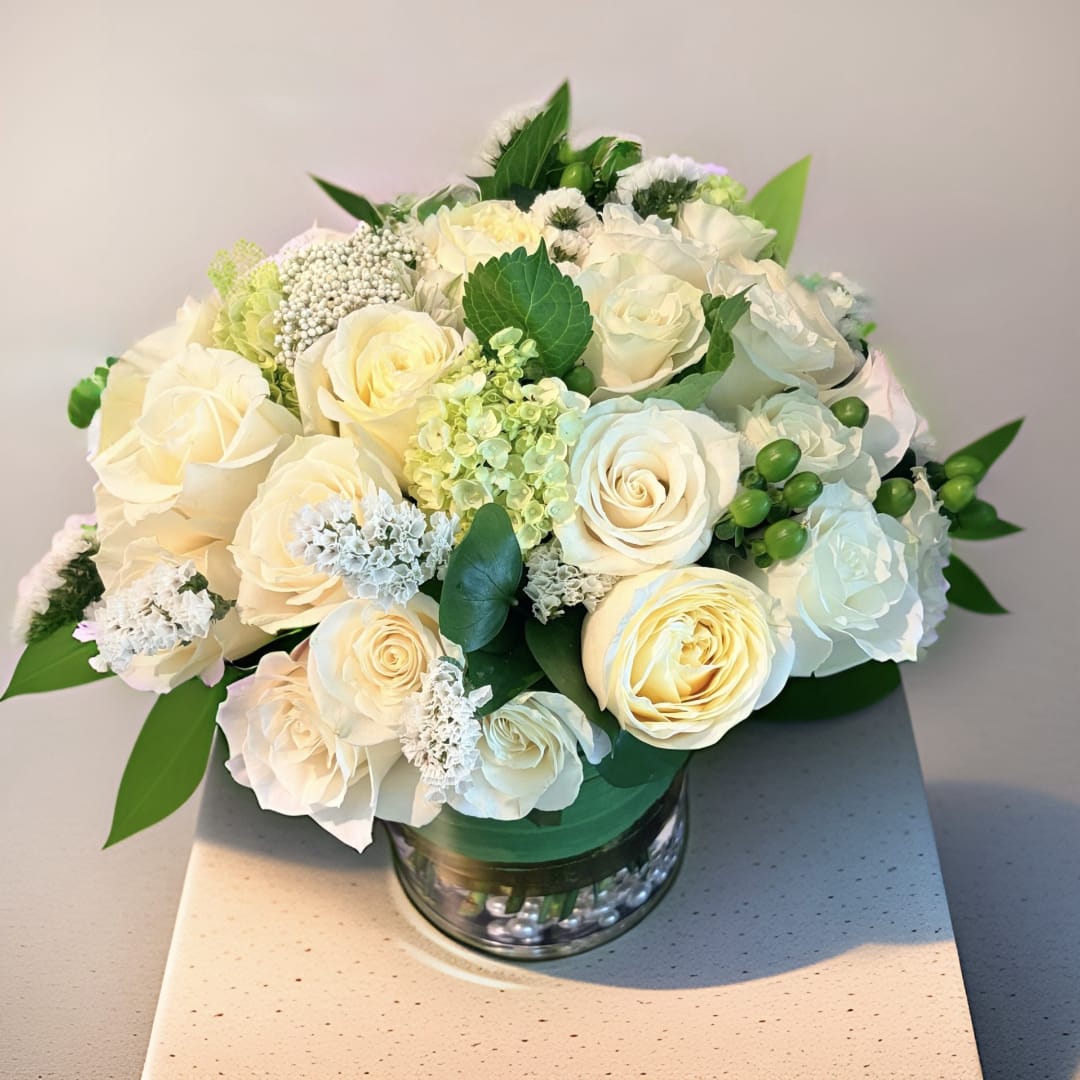 Cream rose bouquet in a glass vase with green accents