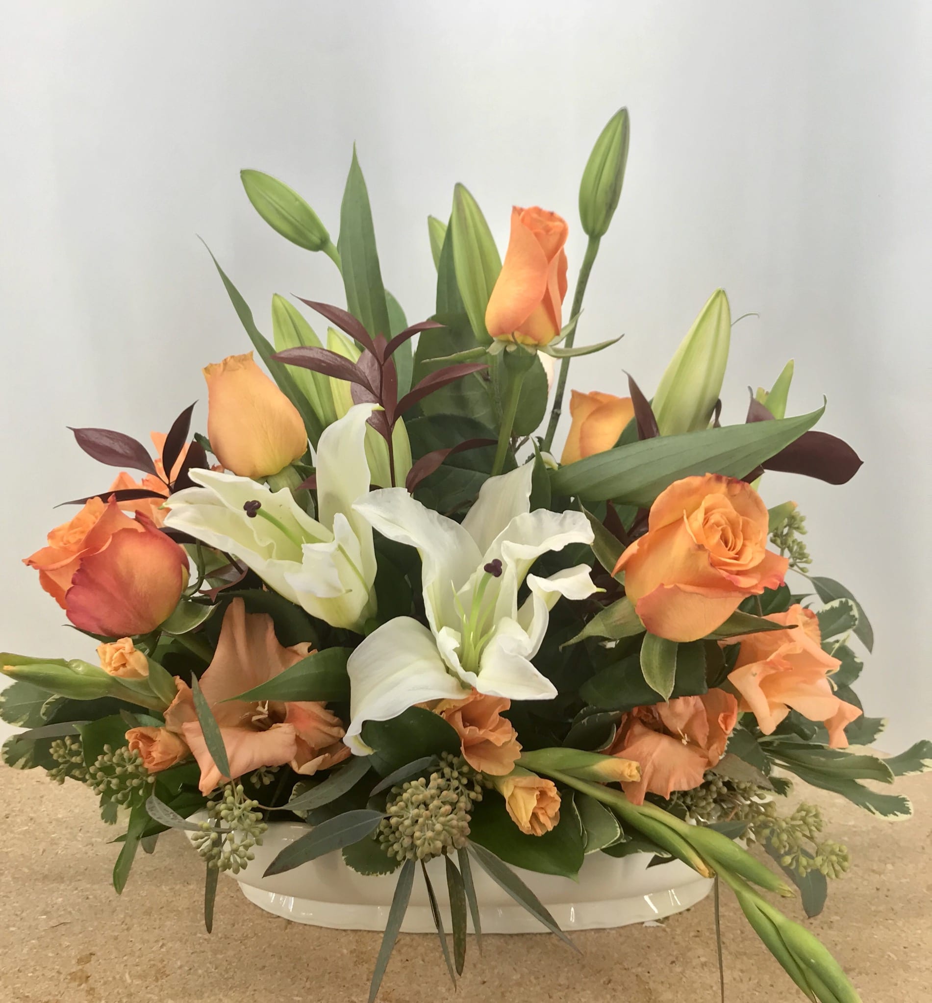 Radiant Glory Arrangement  - A lovely arrangement of white lilies and colorful roses, mixed with an assortment of greenery and presented in a ceramic container, can be used to ornament any at-home or business event. An excellent all-purpose selection. Exact container may vary.