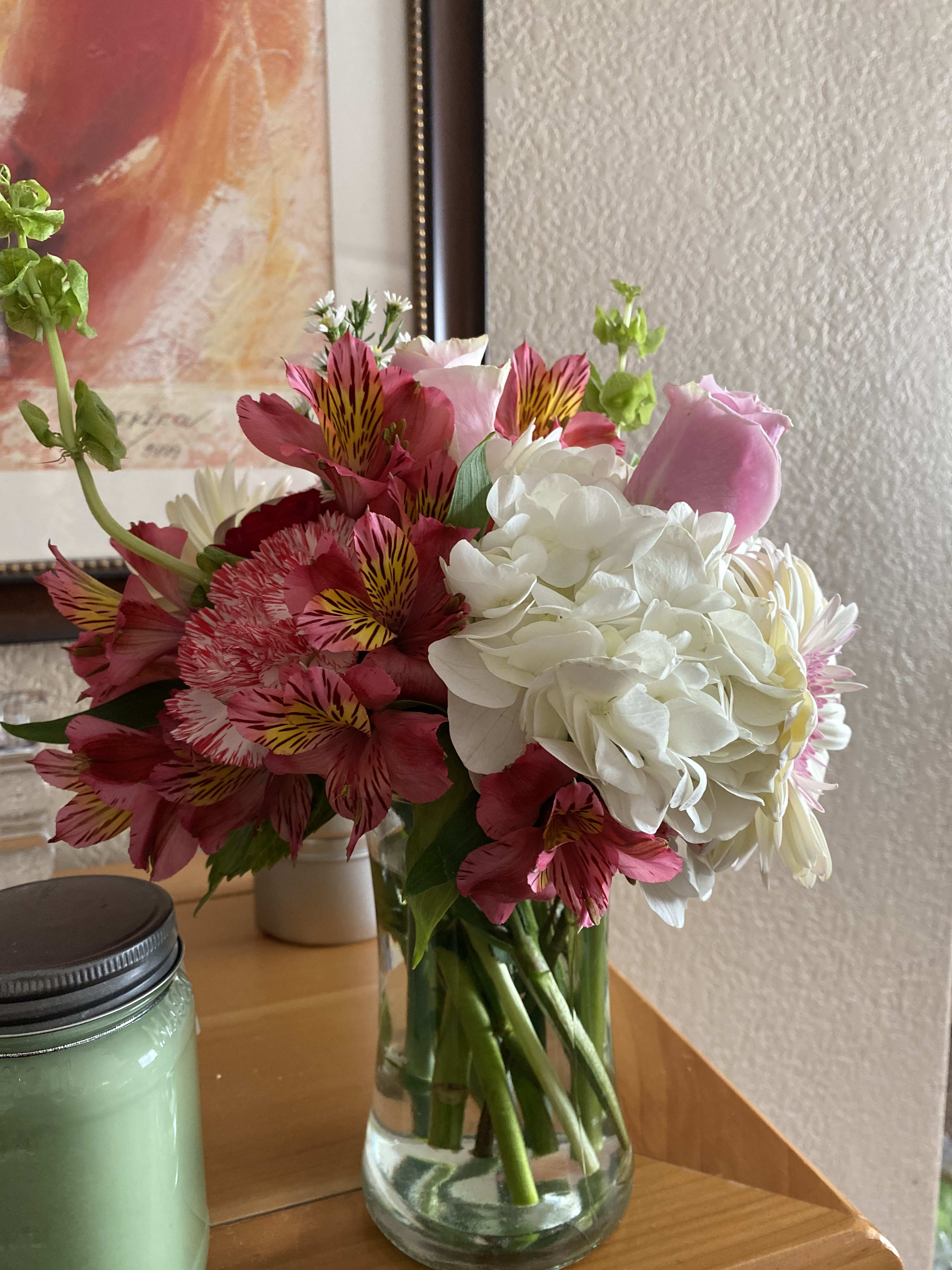 Mixed bouquet of pink alstroemeria, white hydrangeas, and a pink rose in a clear glass vase on a table