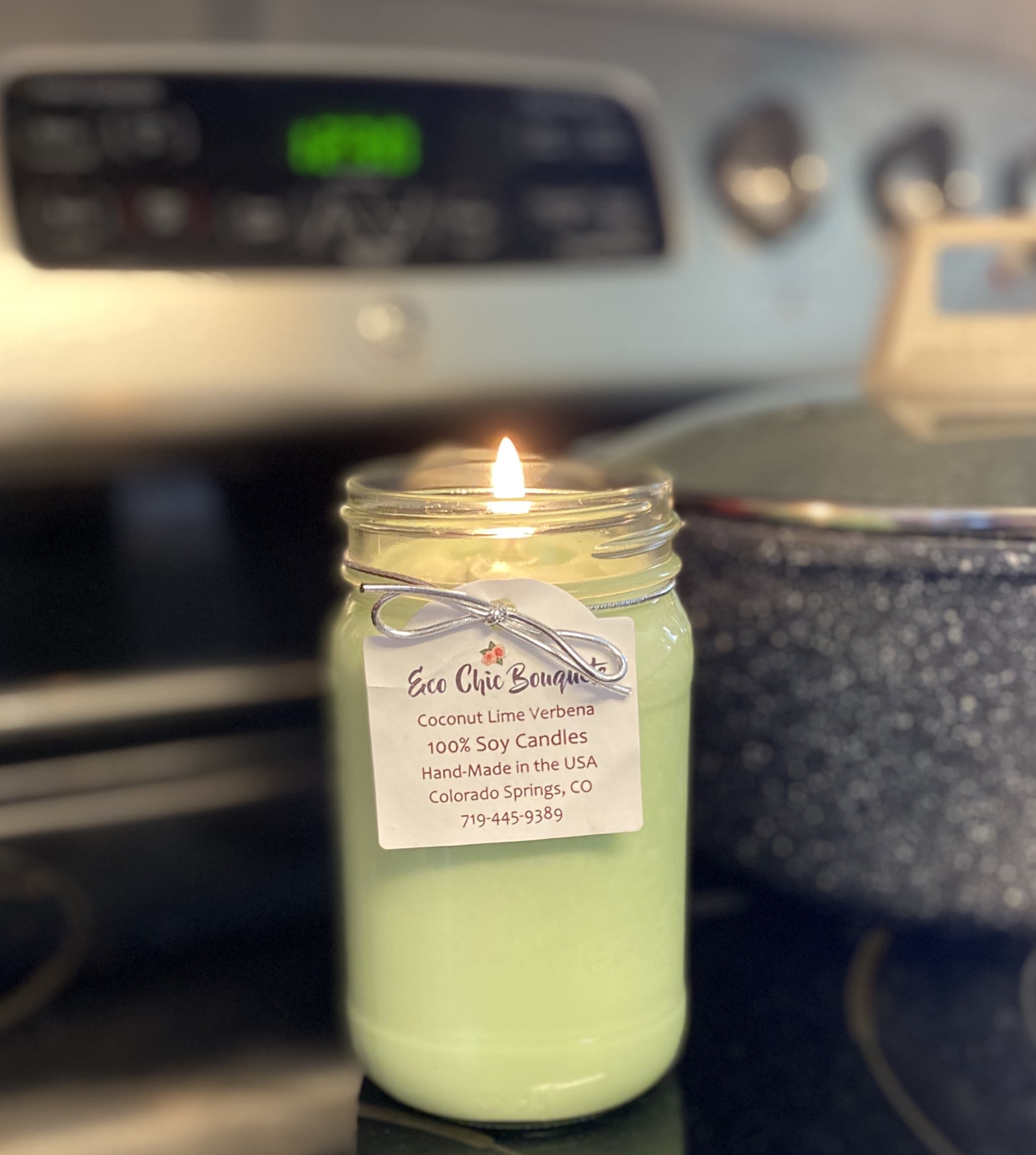 Lit green candle in a glass jar with a hanging label