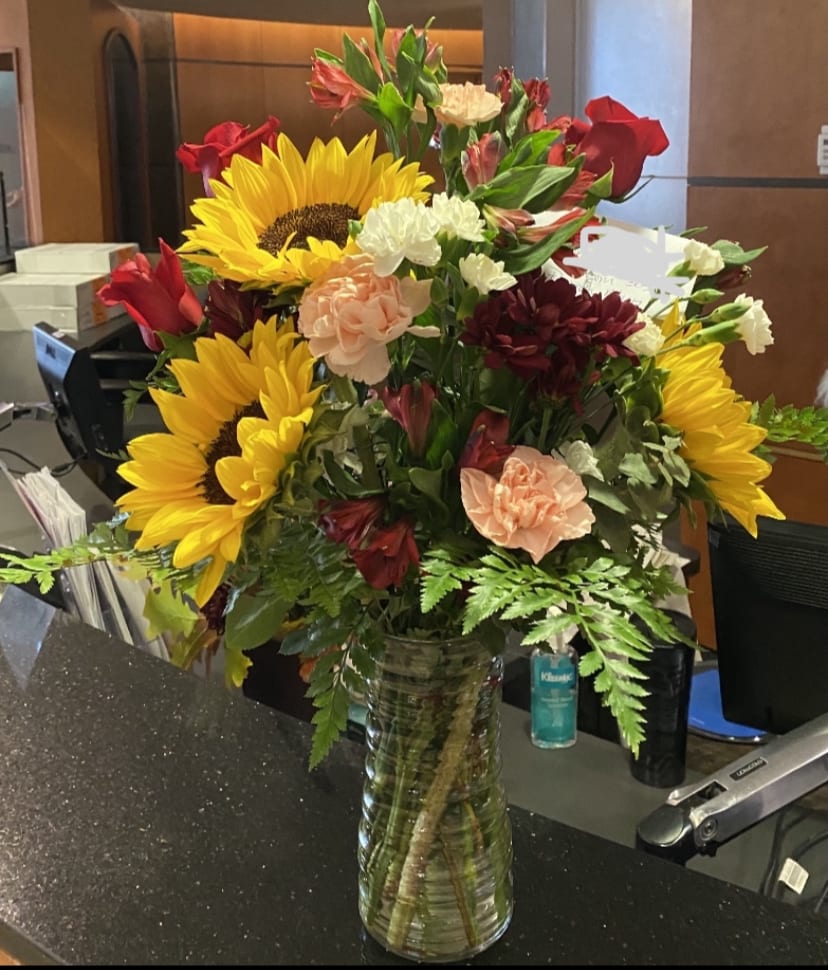 Mixed bouquet with sunflowers, roses, carnations, and alstroemeria in a glass vase