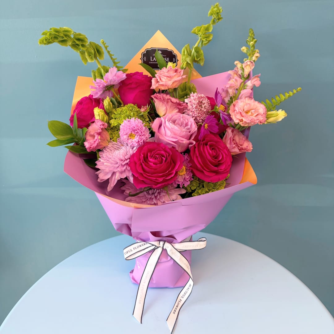 Bouquet of pink and magenta roses with mixed blooms wrapped in pastel paper