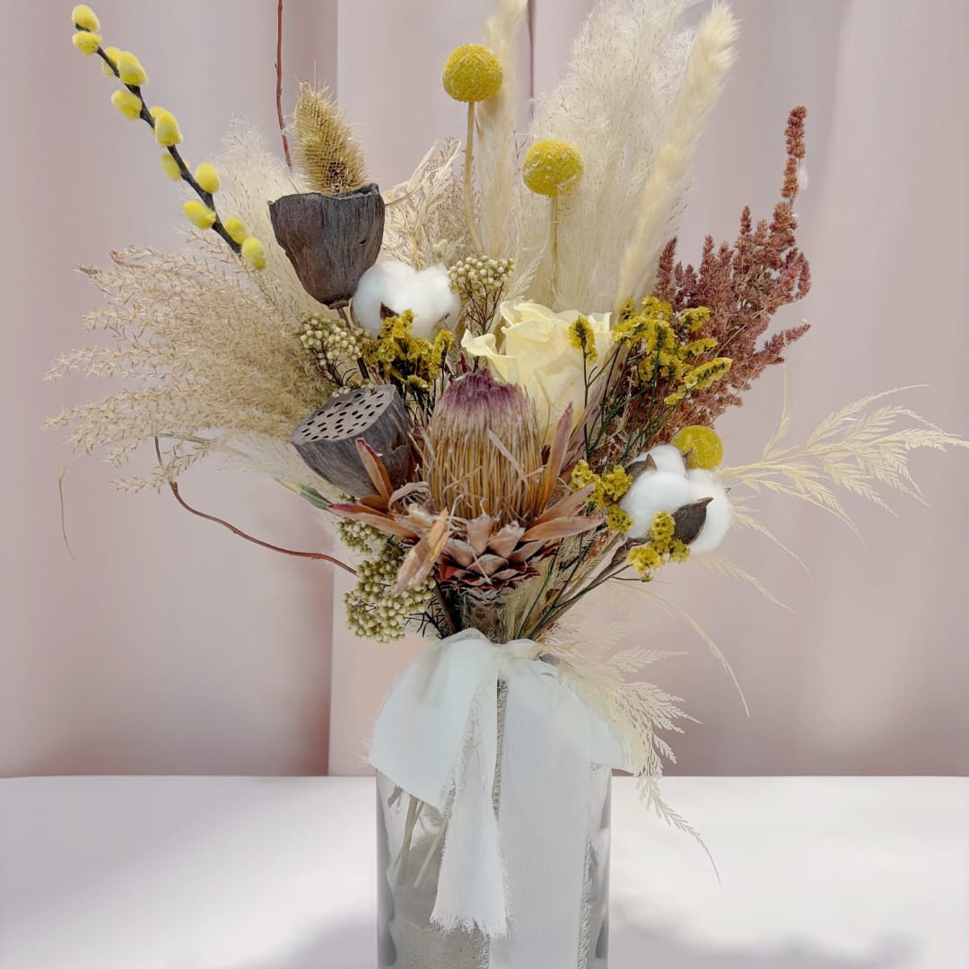 Dried floral arrangement in a clear vase with a white ribbon