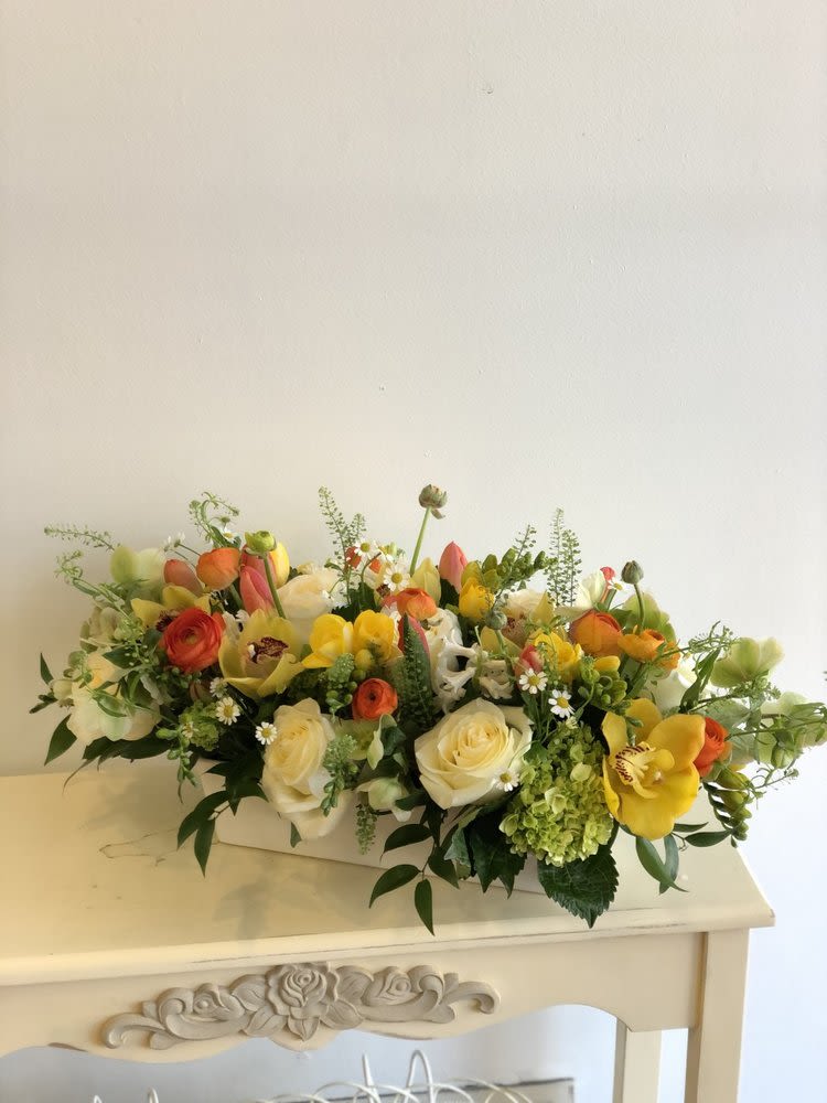 Low floral arrangement with roses, tulips, and ranunculus in a white container