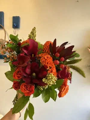 Handheld bouquet of red and orange flowers with green foliage
