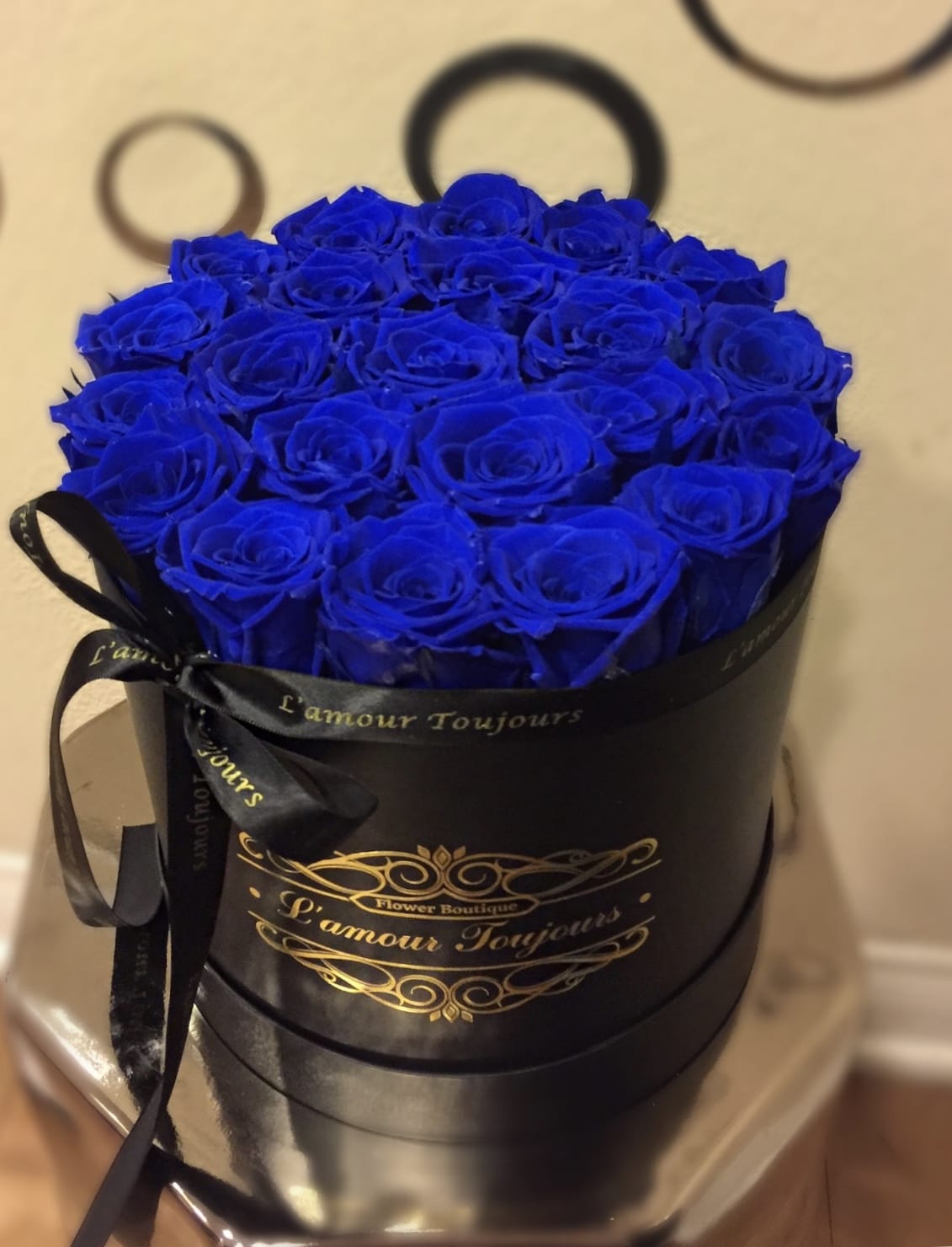 Round black hat box filled tightly with vivid blue roses and tied with a black ribbon