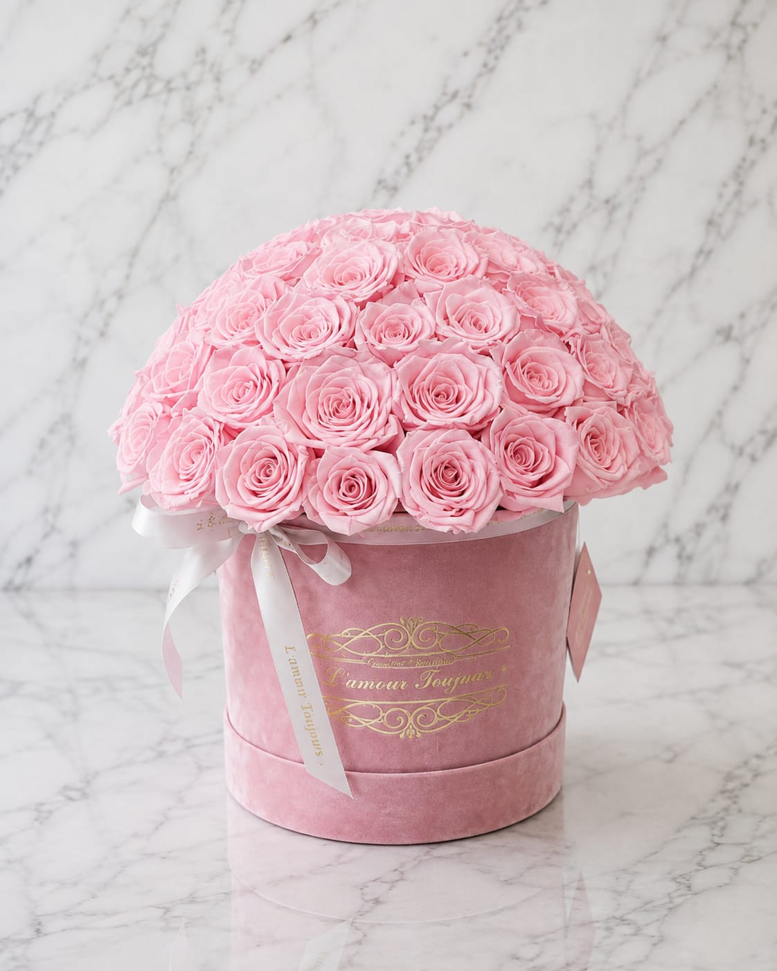 Pink roses arranged in a round velvet hat box with a ribbon