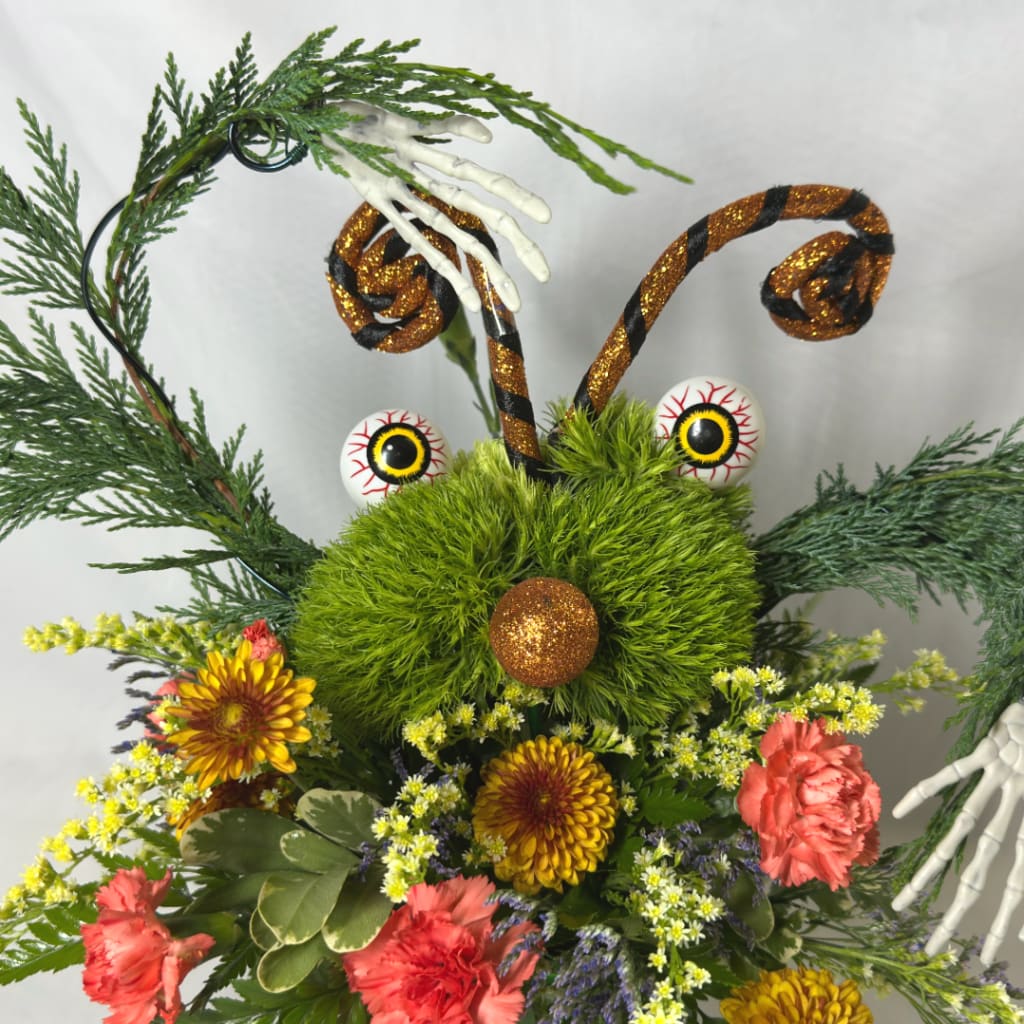 Halloween floral arrangement with a green fuzzy face, glittery antennae, and flowers
