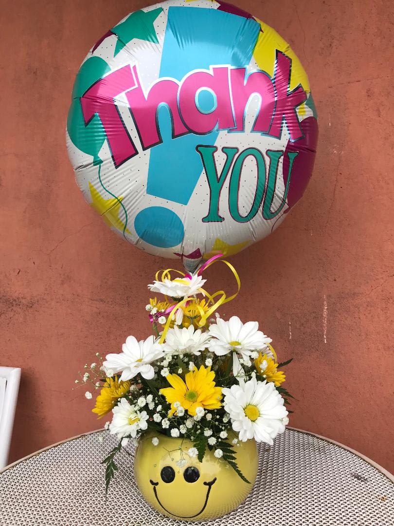 Daisy bouquet in a smiley-face vase with a colorful thank-you balloon
