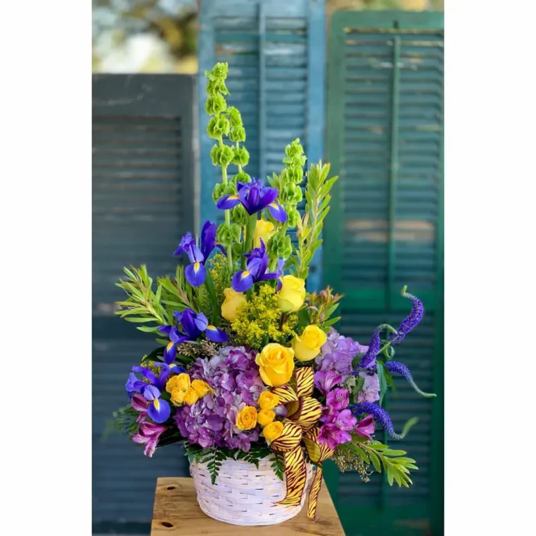 Colorful flower arrangement in a white basket with purple, yellow, and blue blooms