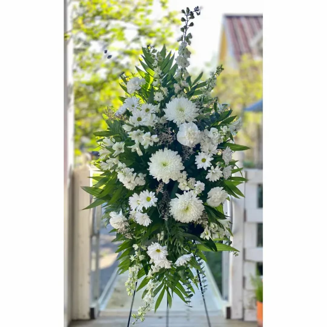 Tall white floral standing spray on an easel with mixed greenery