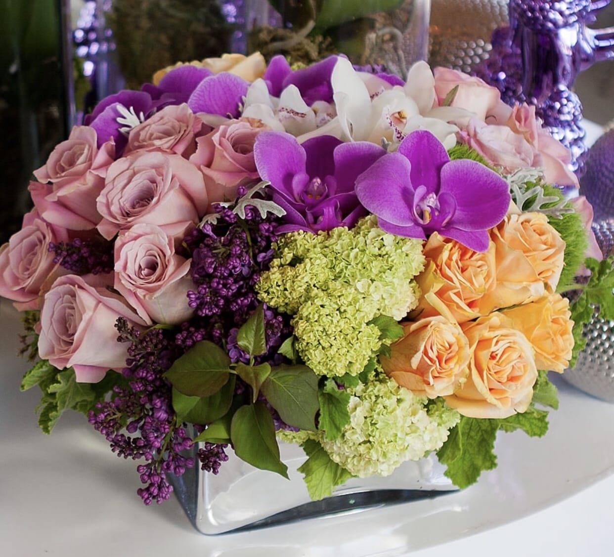 Mixed bouquet of pink roses, purple orchids, and white flowers in a glass vase