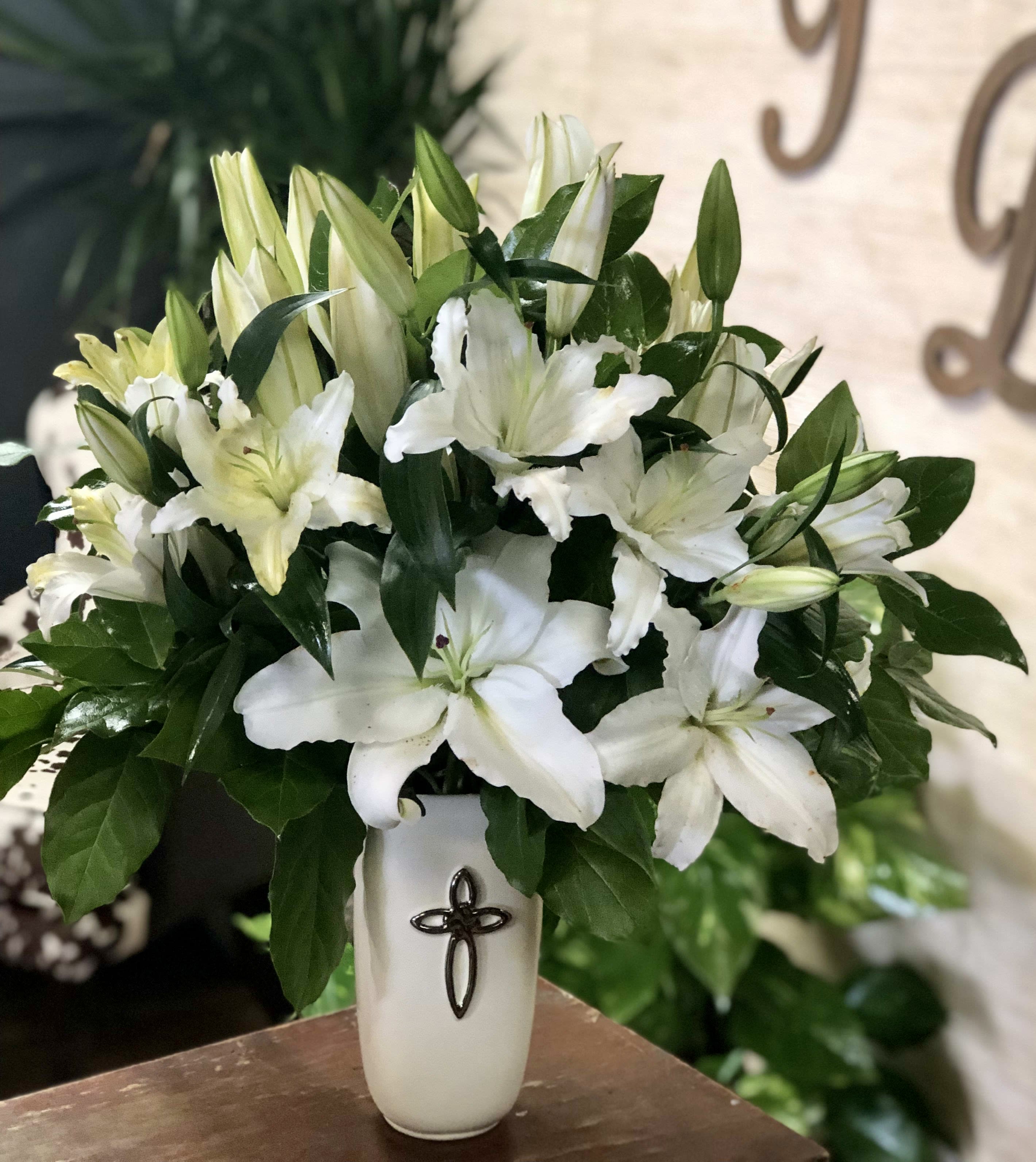White lilies arranged in a white vase with a cross emblem