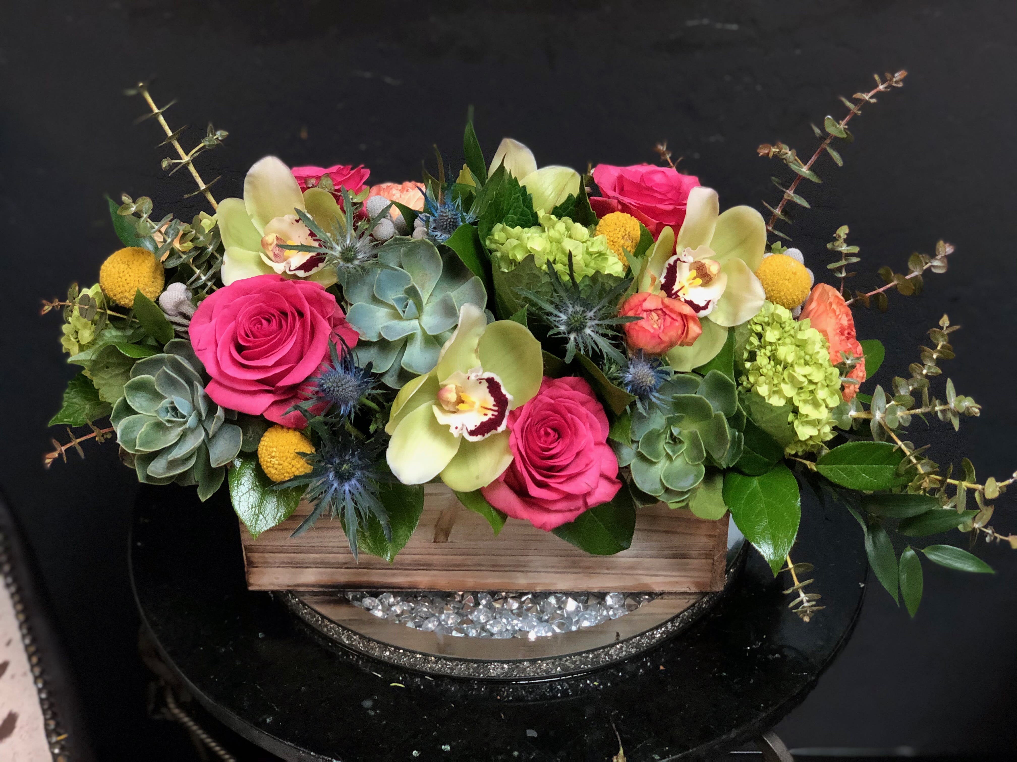Pink roses and pale orchids in a wooden box with succulents