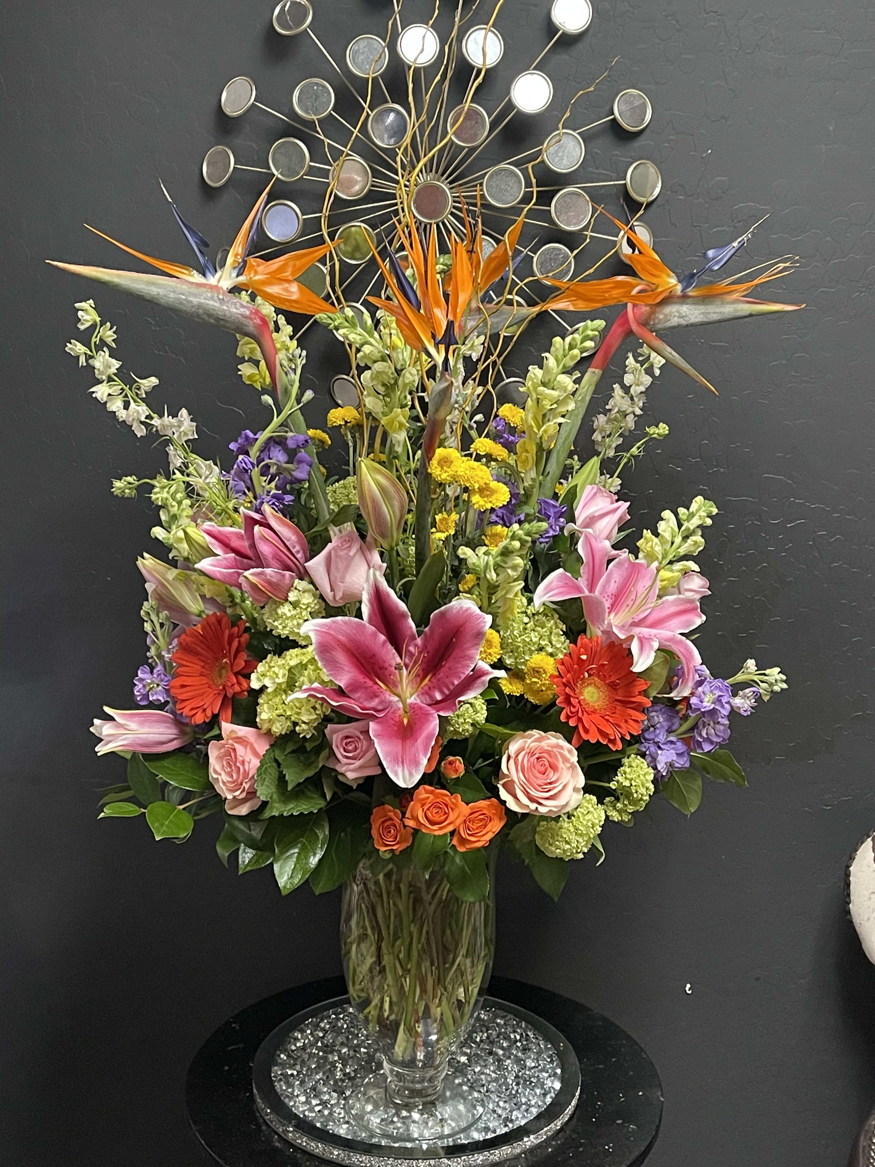 Tall mixed bouquet in a glass vase with pink lilies, roses, and orange birds of paradise