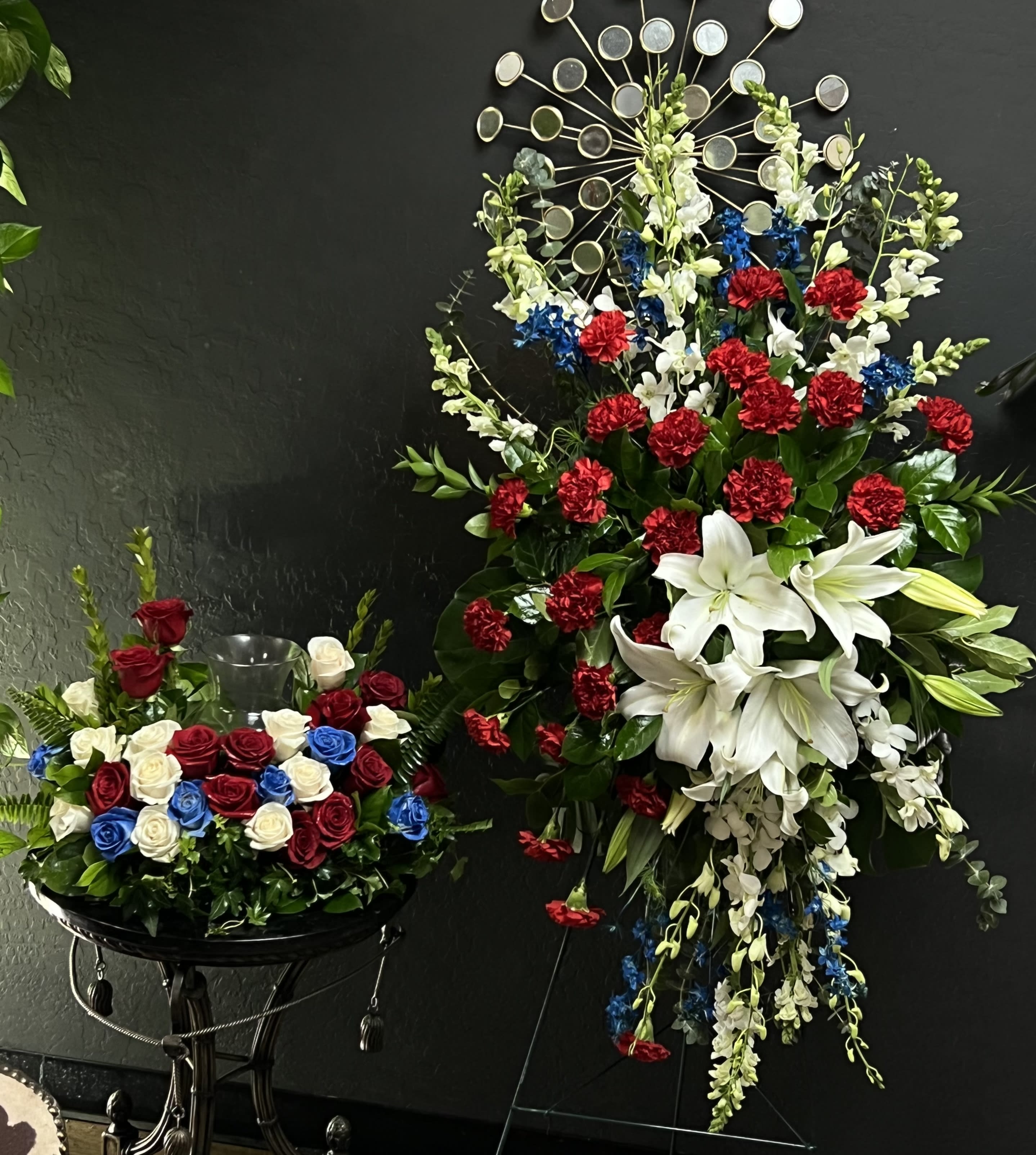 Two floral arrangements with red, white, and blue flowers on black stands.