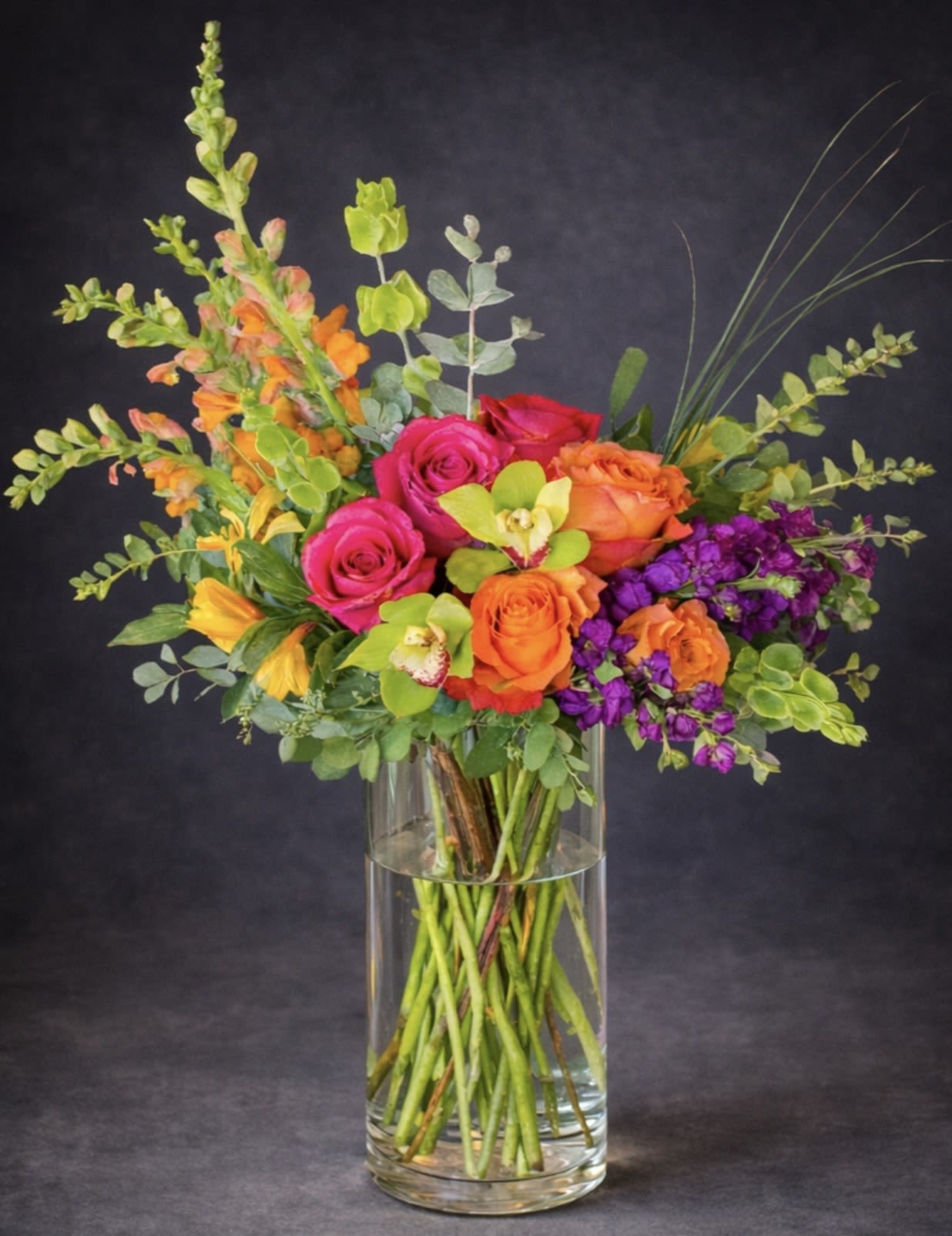 Colorful bouquet of roses, orchids, and snapdragons in a clear glass vase