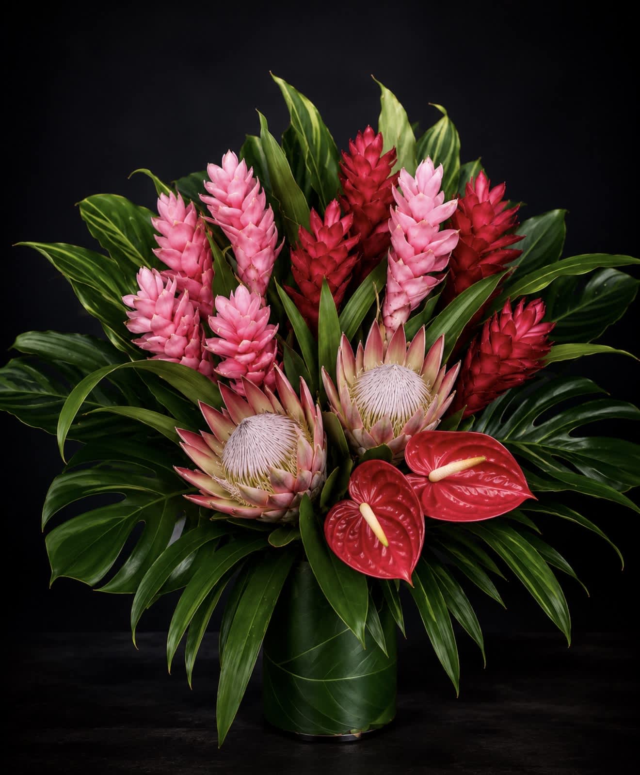 Tropical arrangement with pink and red blooms in a green vase
