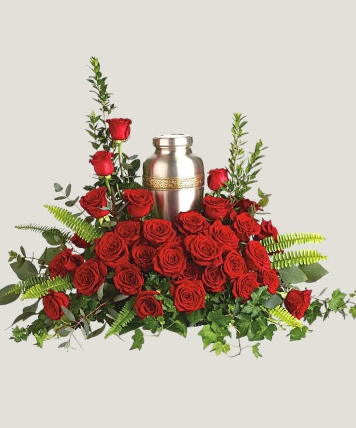 Red roses arranged around a silver urn with greenery