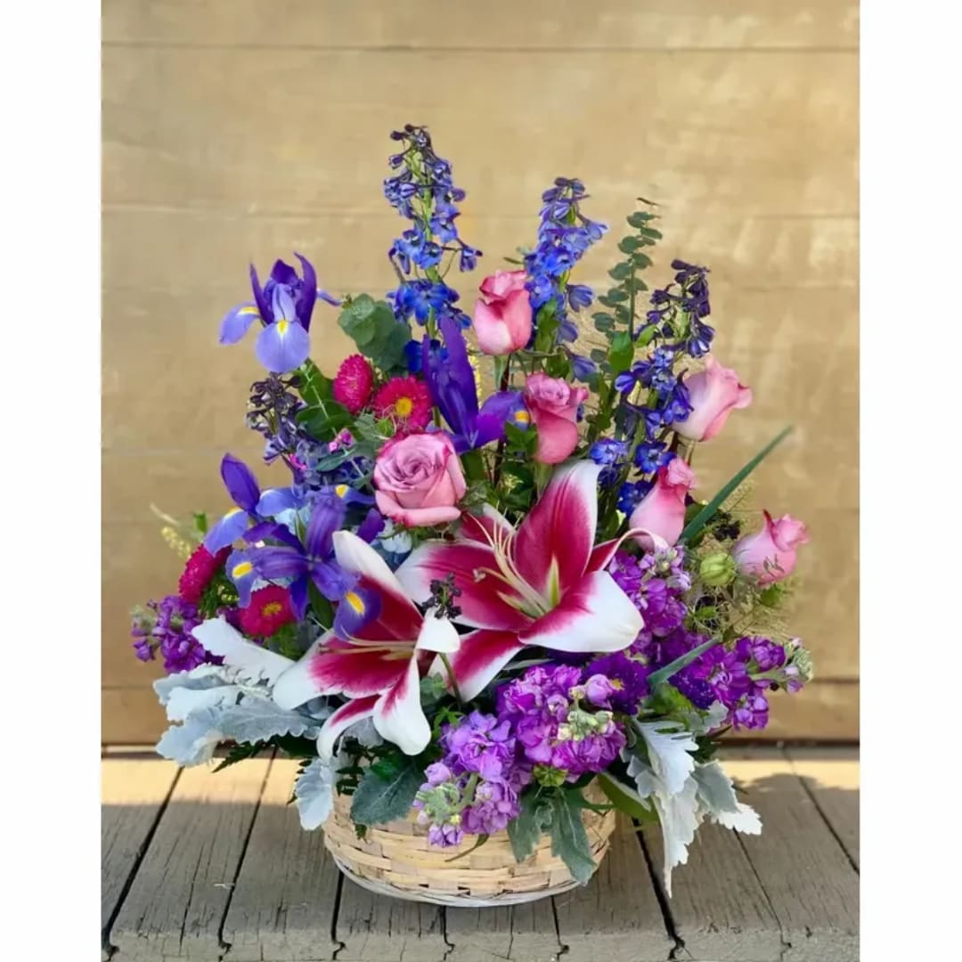 Basket arrangement with pink roses, purple lilies, and blue flowers