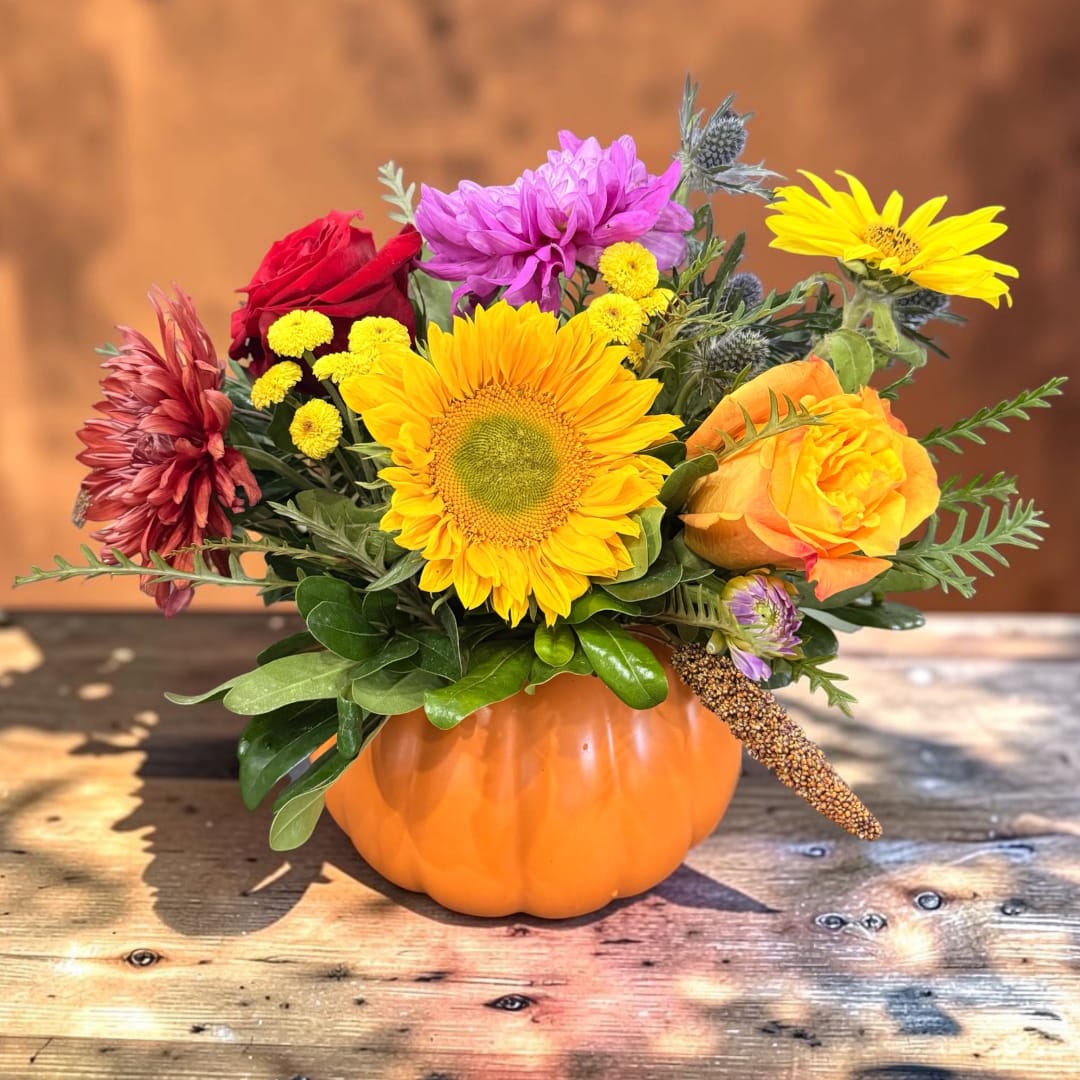 Mixed bouquet in an orange pumpkin container with sunflowers and roses