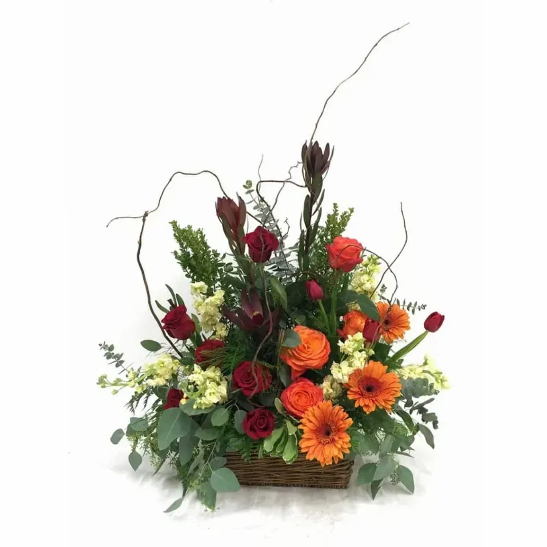 Basket arrangement of red roses and orange gerbera daisies with tall branches