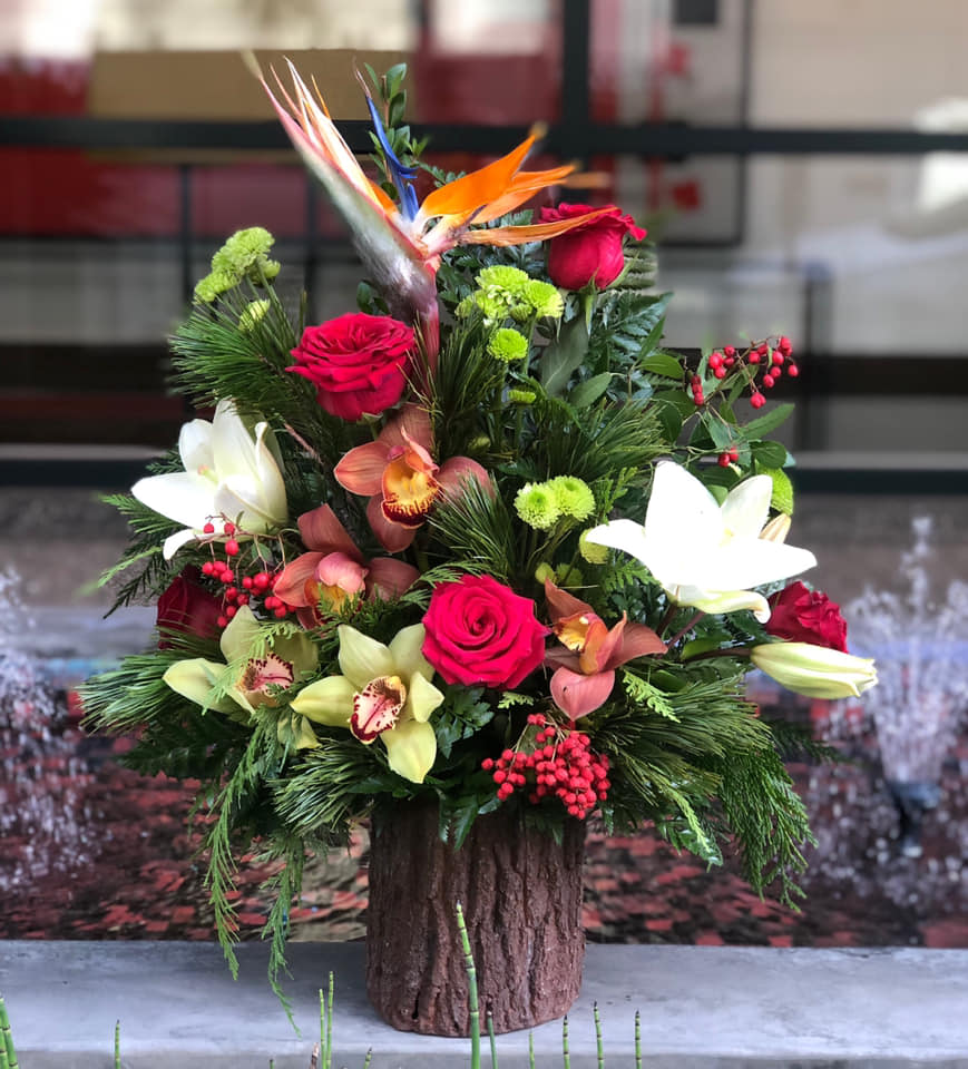 Tropical floral arrangement with roses, lilies, and orchids in a wood-look container