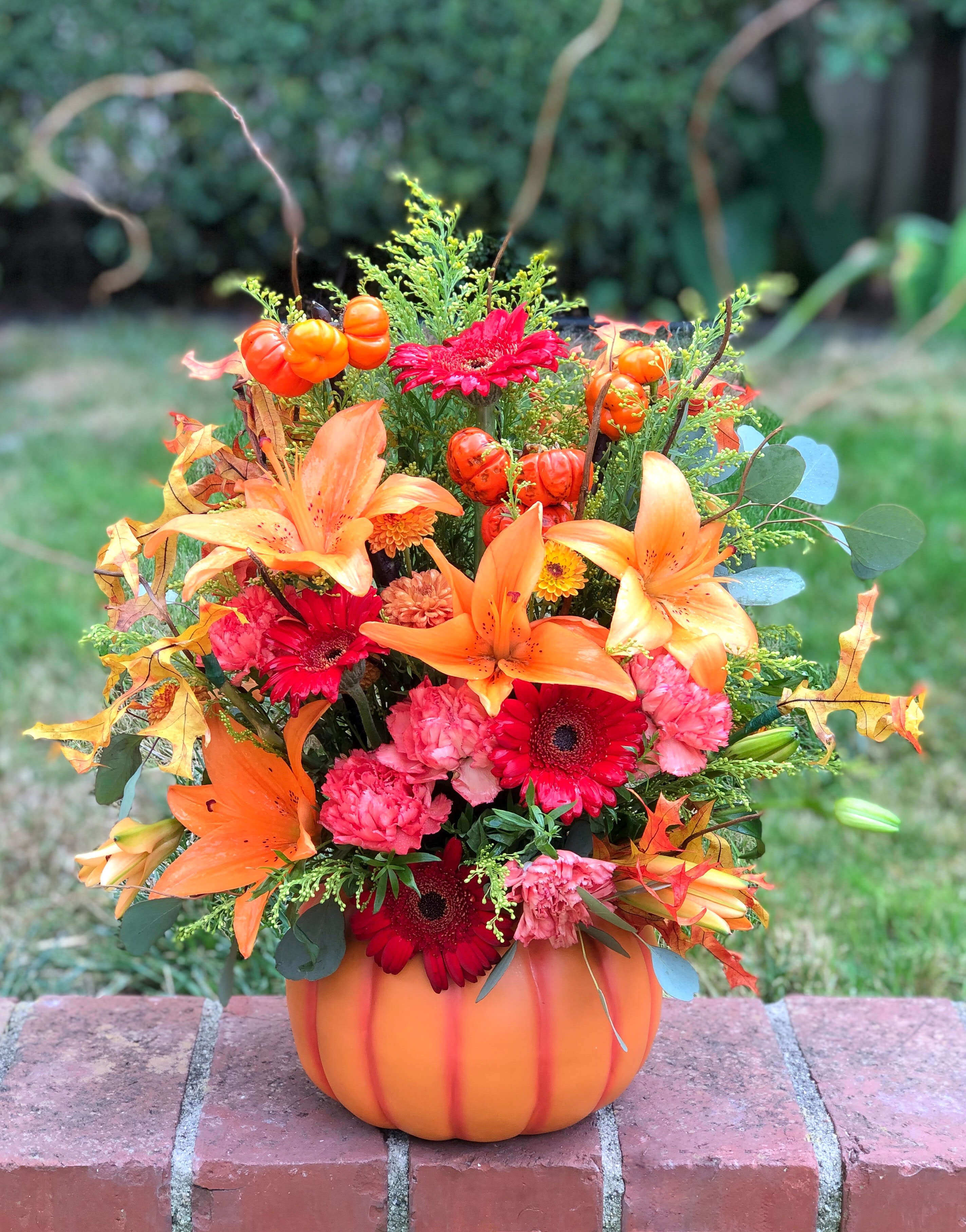 Autumn floral arrangement in a pumpkin-shaped container with orange lilies and red daisies