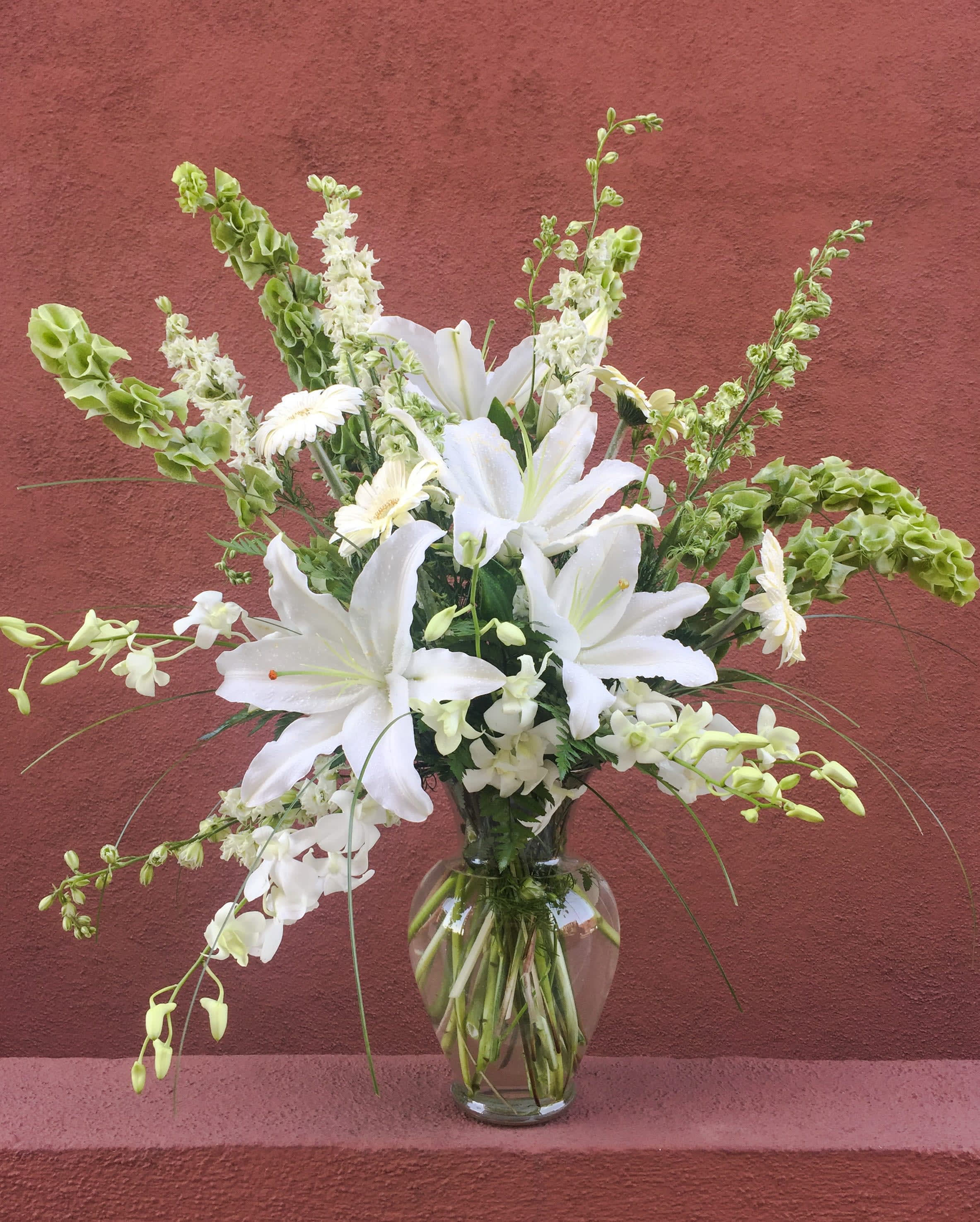 White lilies and orchids arranged in a clear glass vase