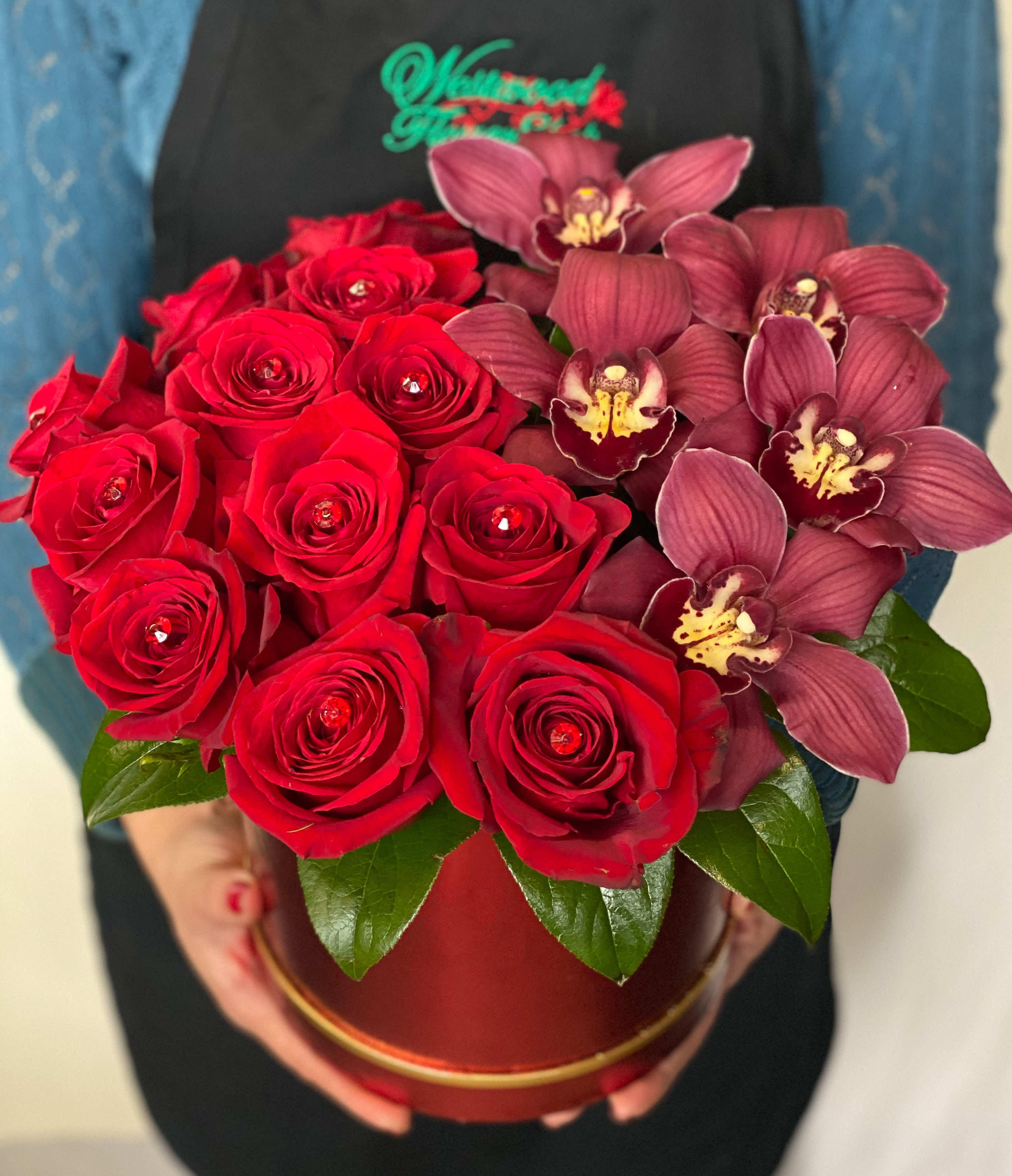 Red roses and burgundy orchids arranged in a round box