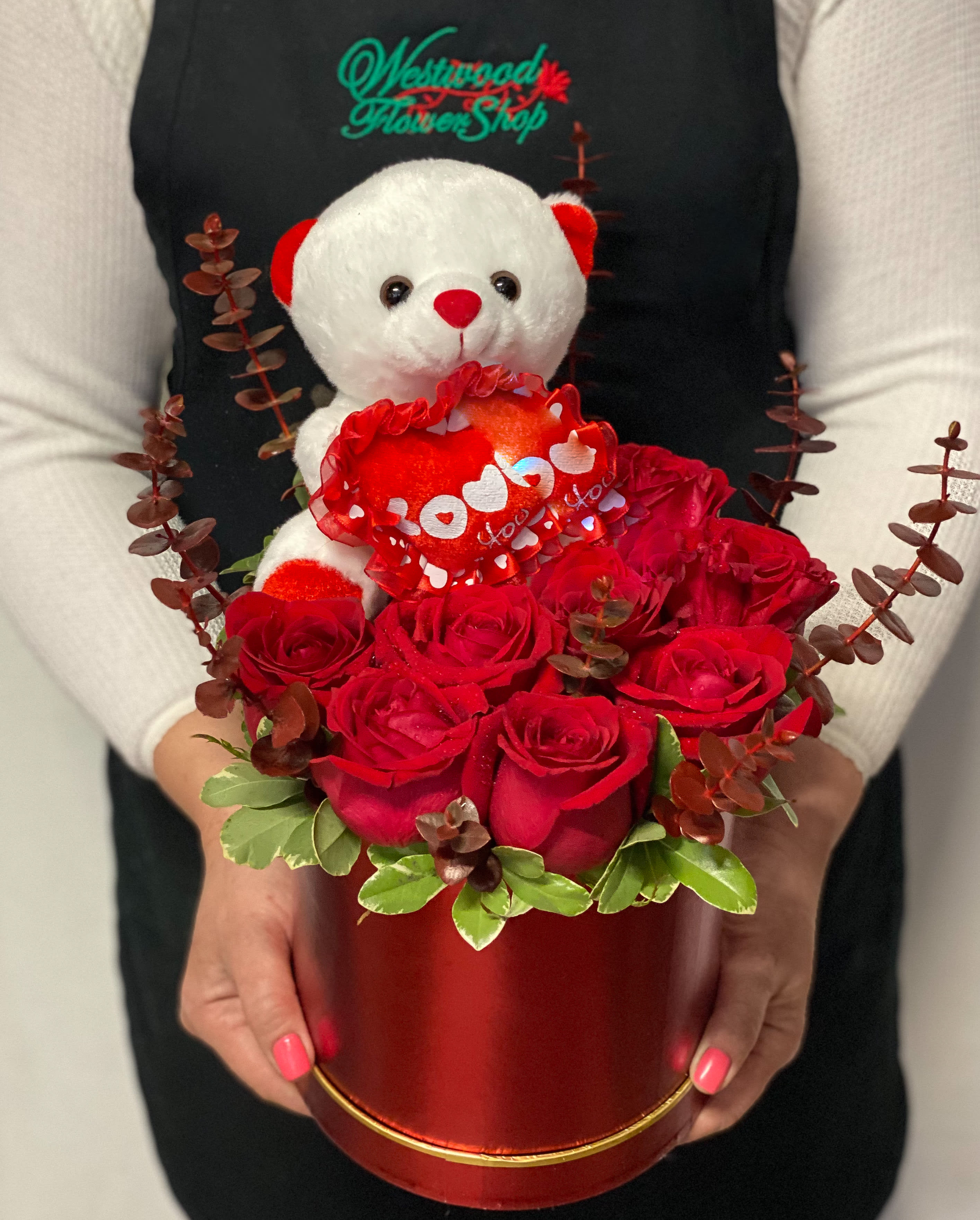 Red roses in a round box with a teddy bear holding a heart