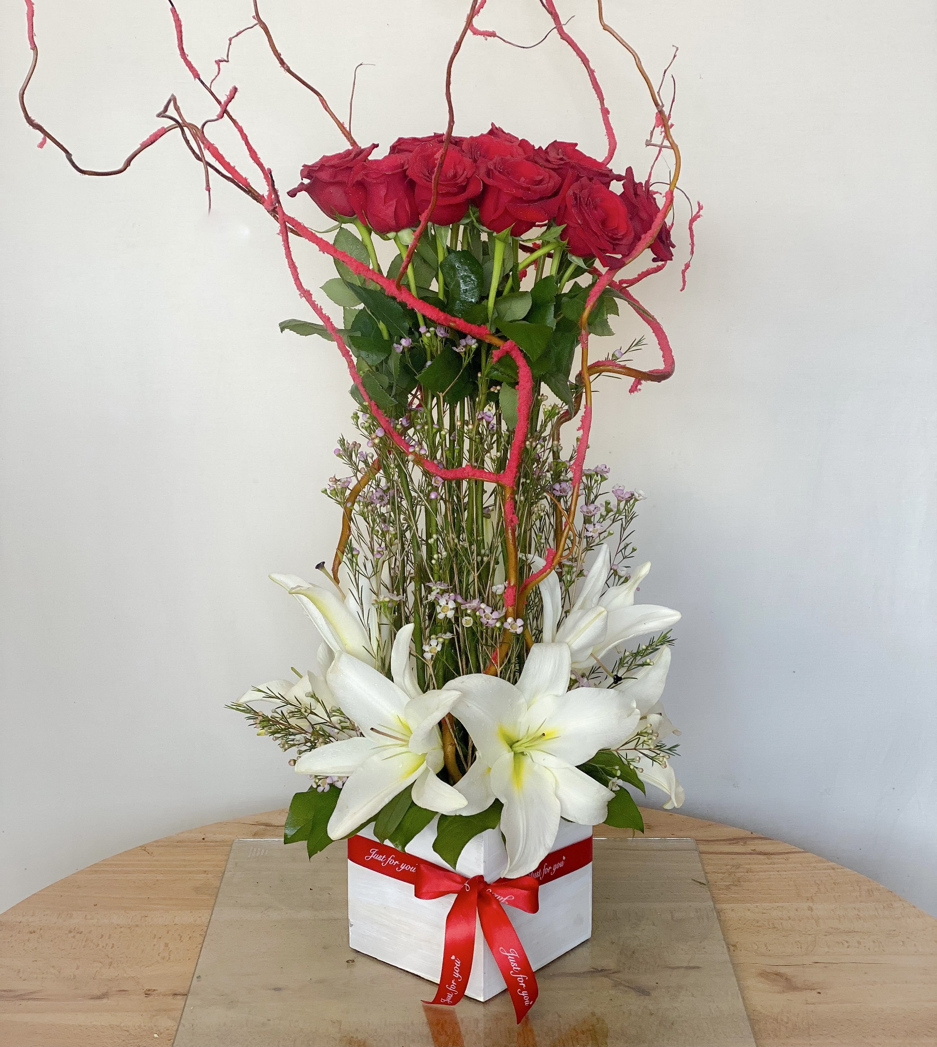 Tall arrangement of red roses and white lilies in a white box with a red ribbon