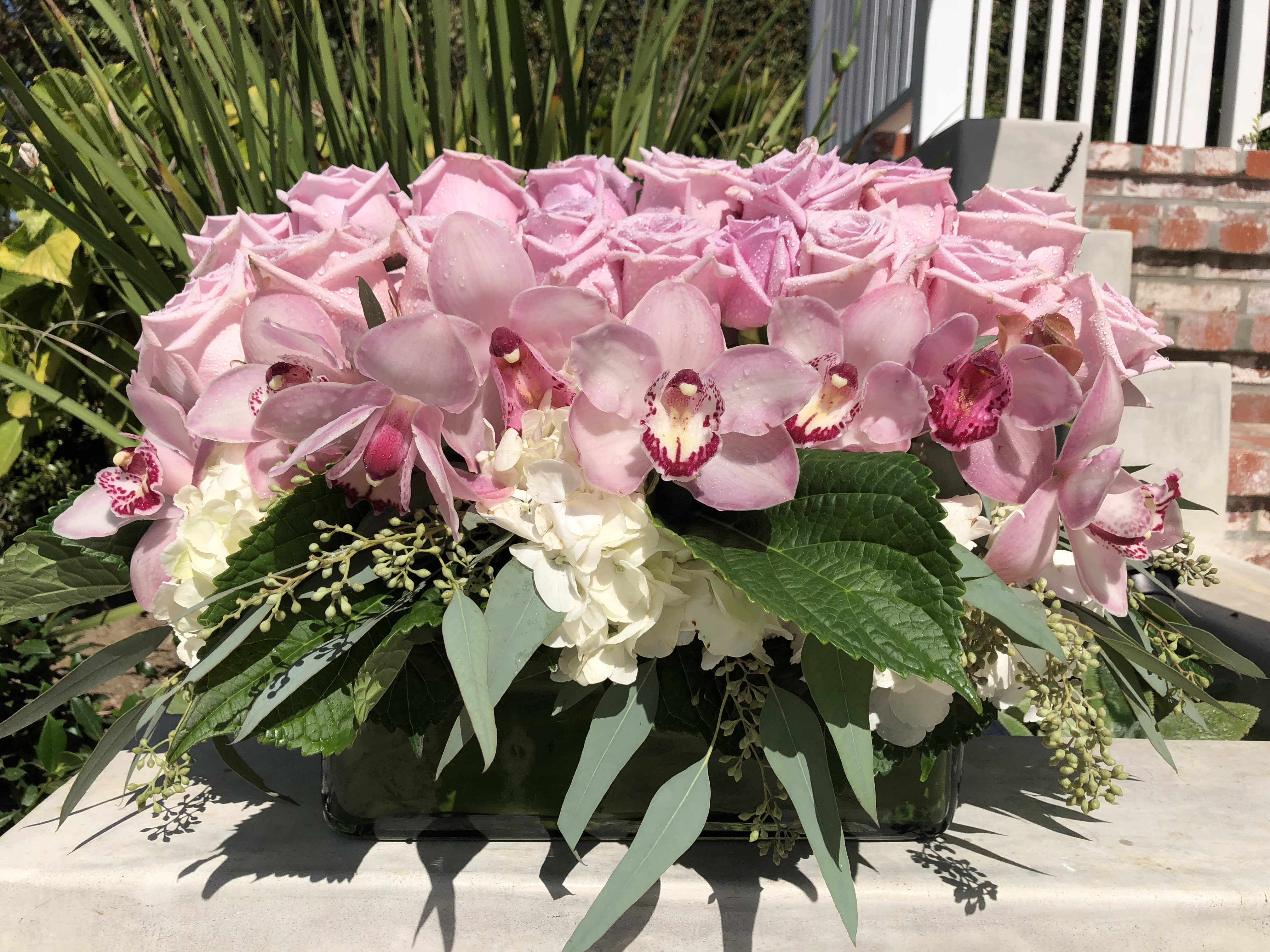 Pink roses and orchids arranged in a low rectangular vase