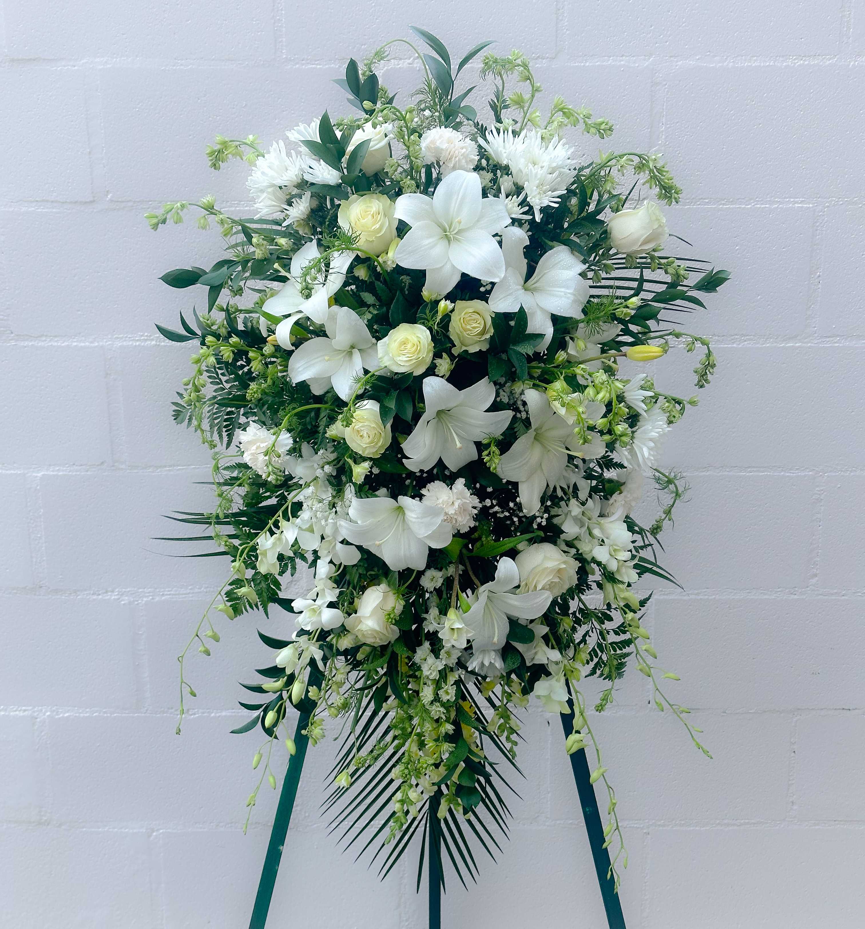 White floral standing spray with lilies and roses on a green easel